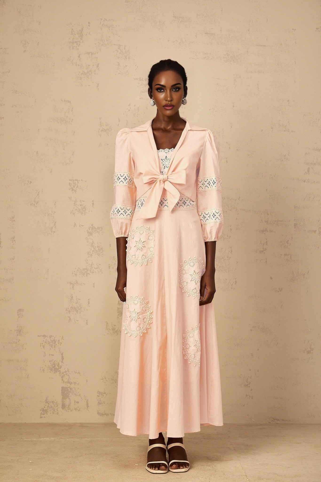 A young girl wearing a pink blouse and dress set with delicate floral embroidery the blouse has short puffed sleeves and the dress features a matching floral pattern
