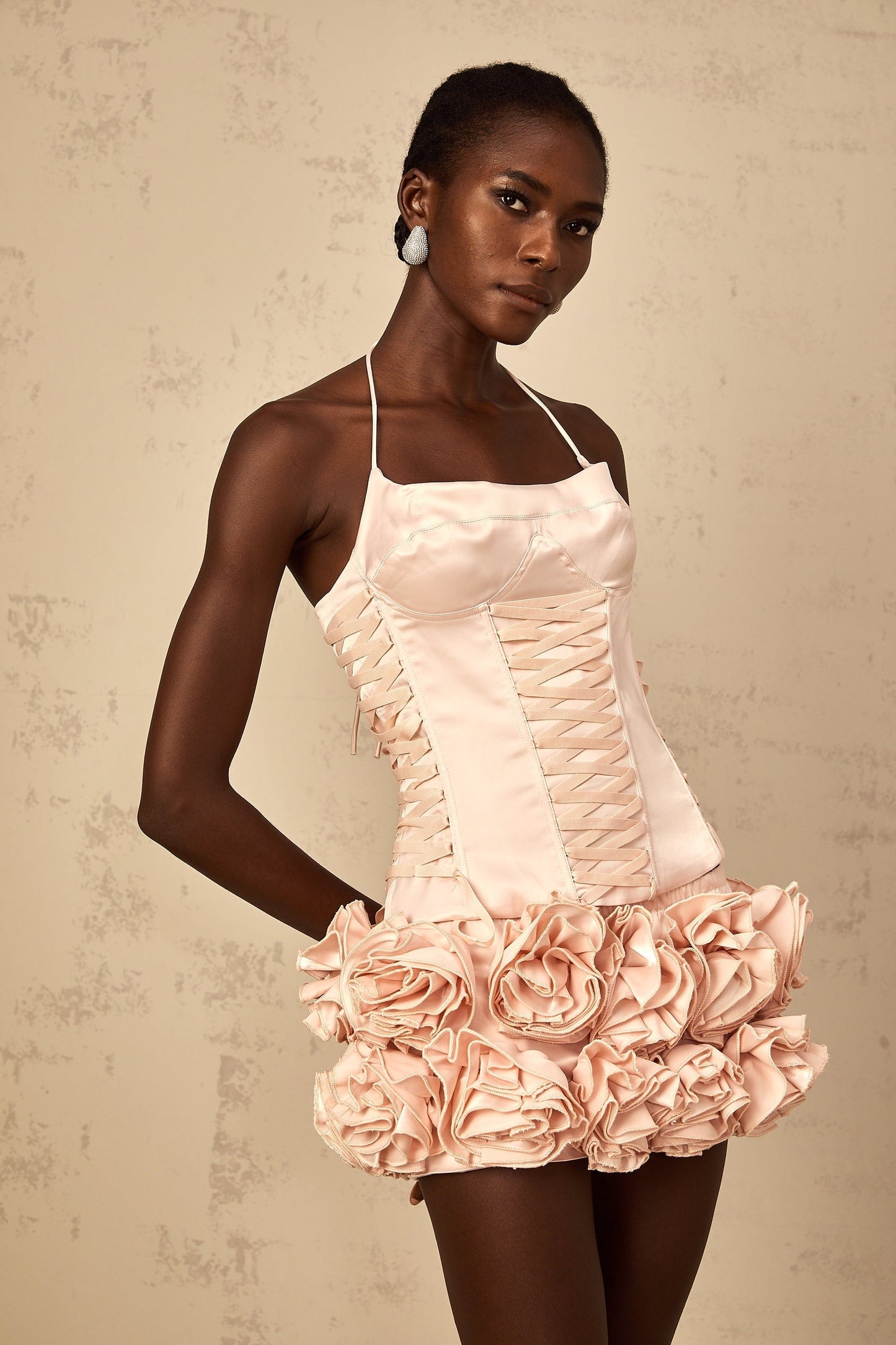 A young woman wearing a pink twopiece outfit consisting of a laceup top and matching skirt adorned with faux flower embellishments The set has a romantic and feminine style