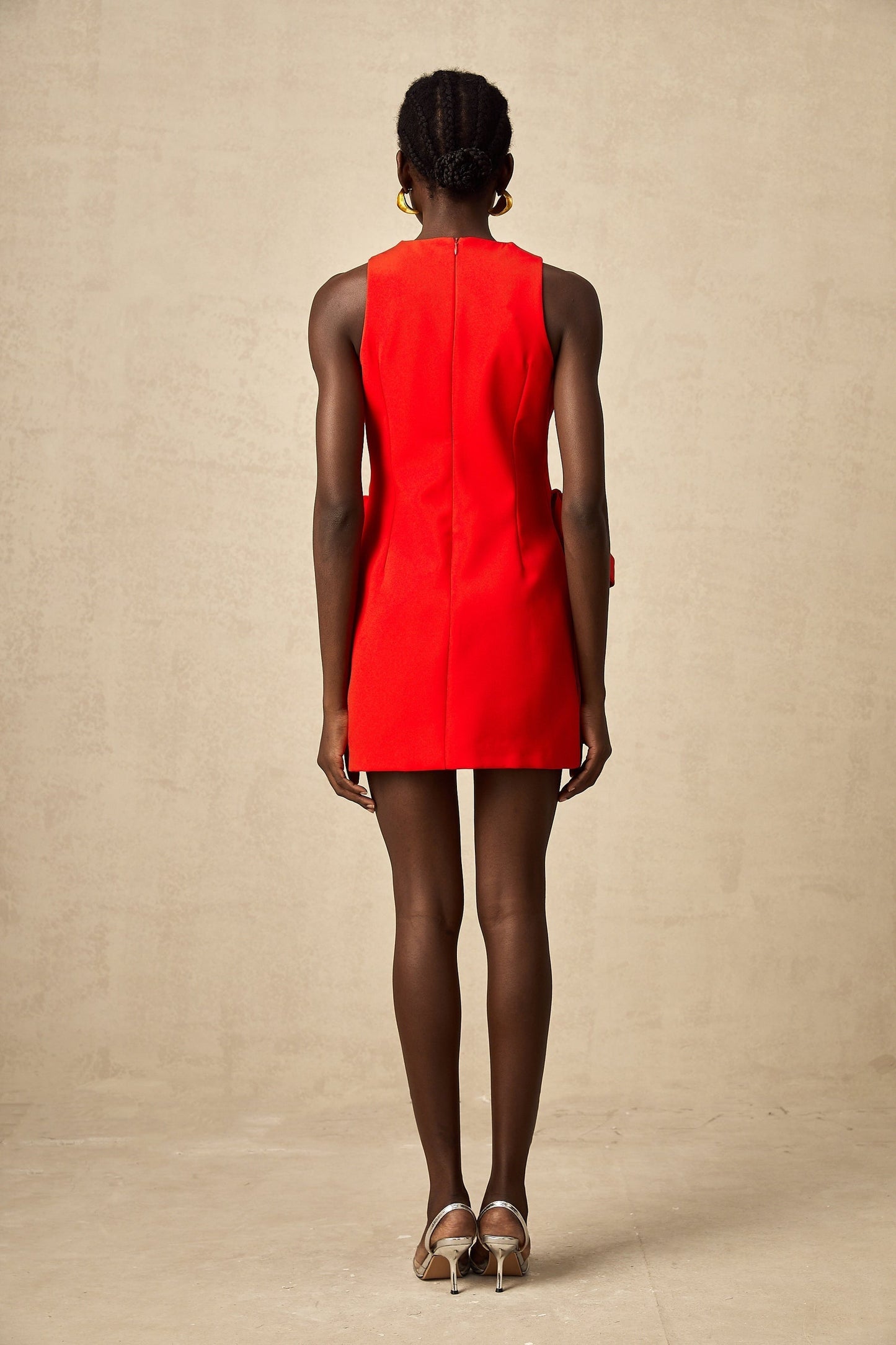 A young woman wearing a sleeveless red mini dress with a bow detail standing in a casual pose