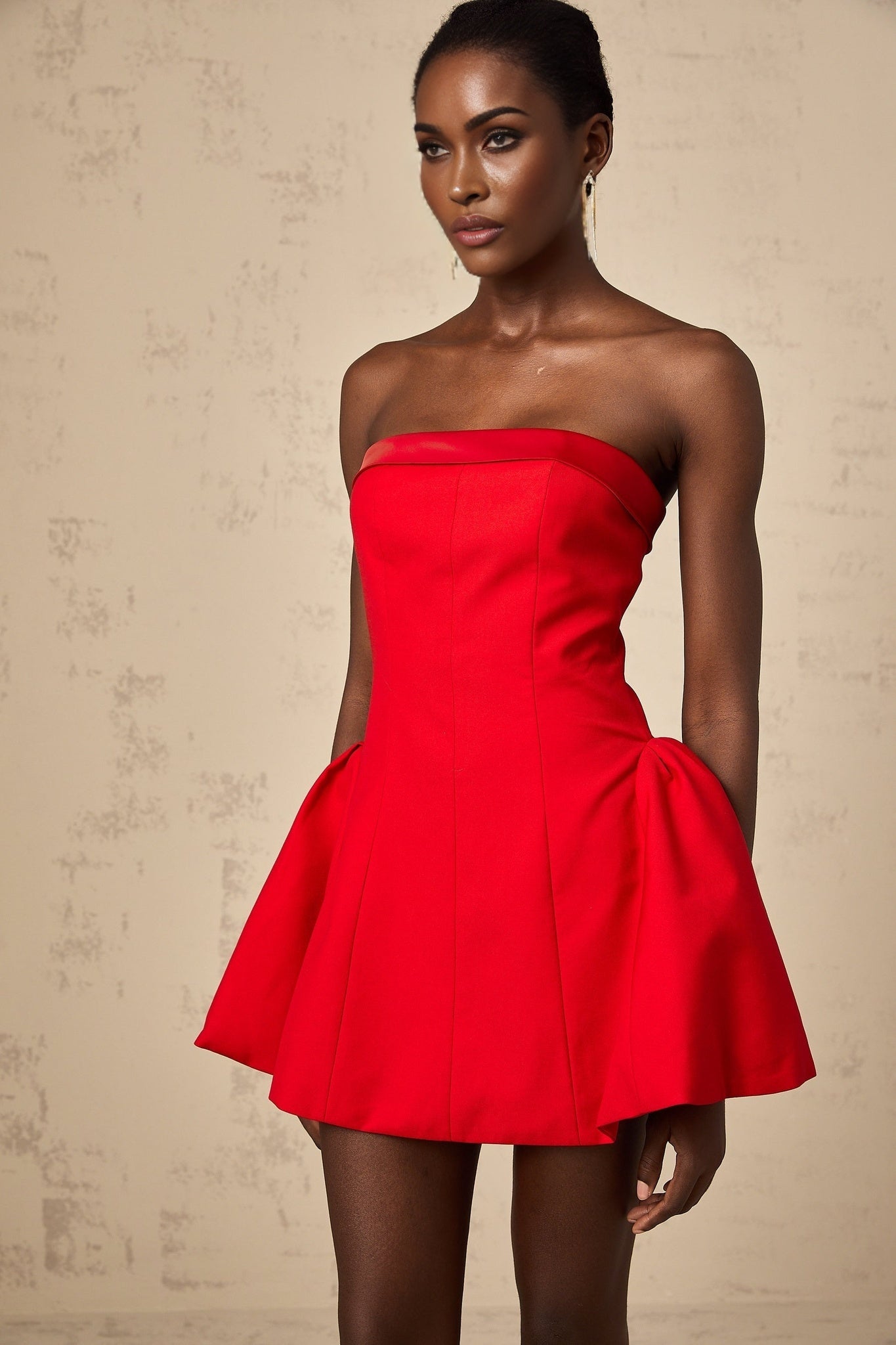 A young woman wearing a vibrant red offshoulder mini dress with flared sleeves and a flared skirt The dress has a fitted bodice and falls above the knee The model is posing against a plain background showcasing the Perrine dress design