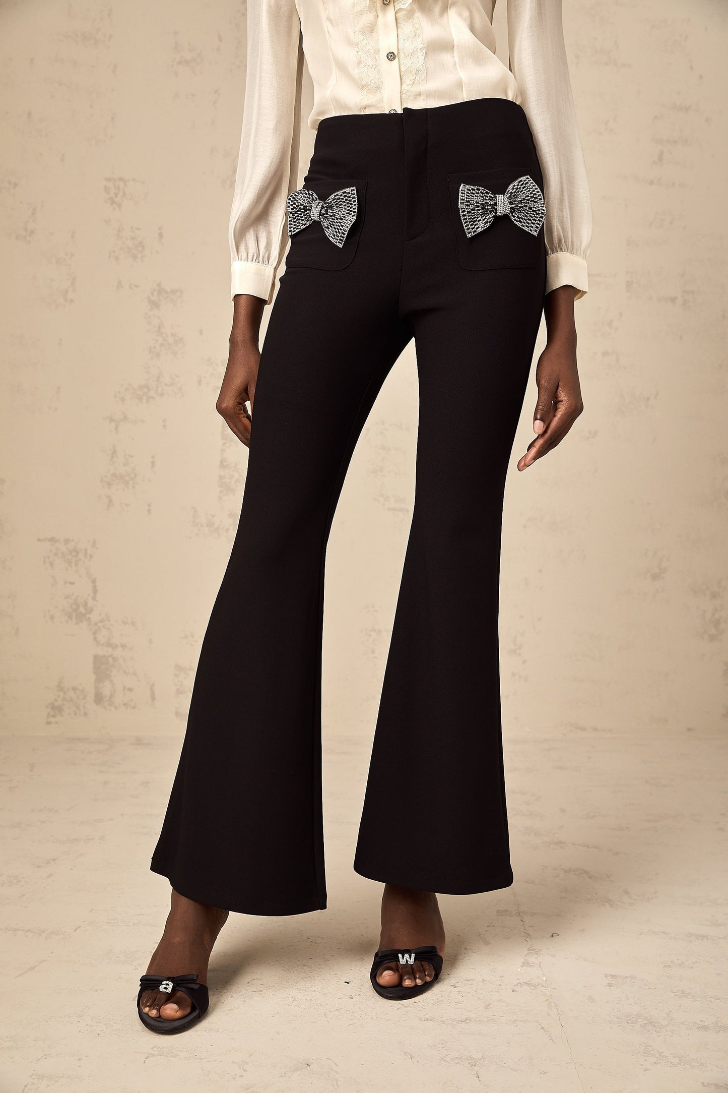 Black flared trousers with large decorative bow detail at waist
