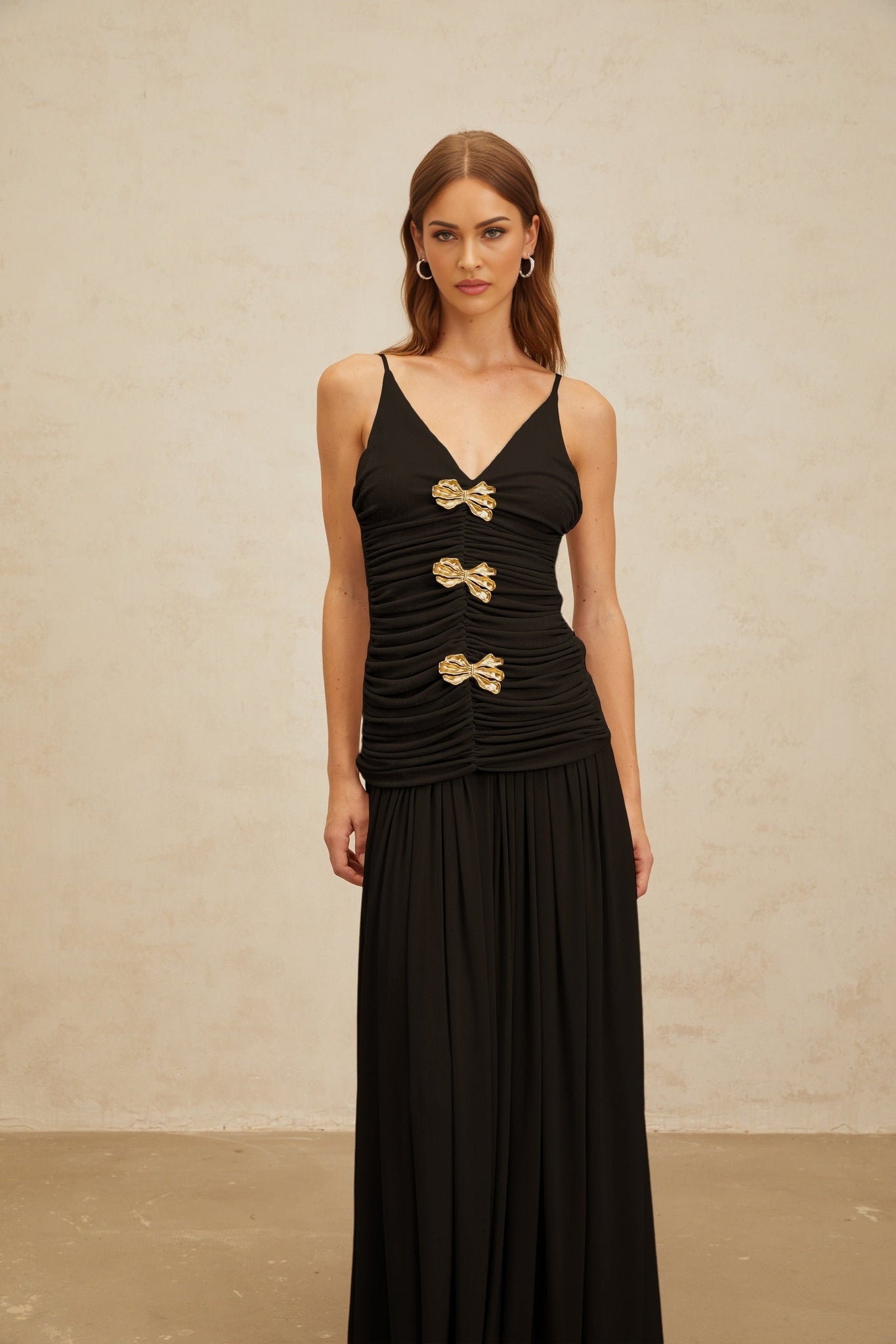 Black sleeveless V-neck top with brooch and ruched detailing and adjustable spaghetti straps, paired with black pleated maxi skirt