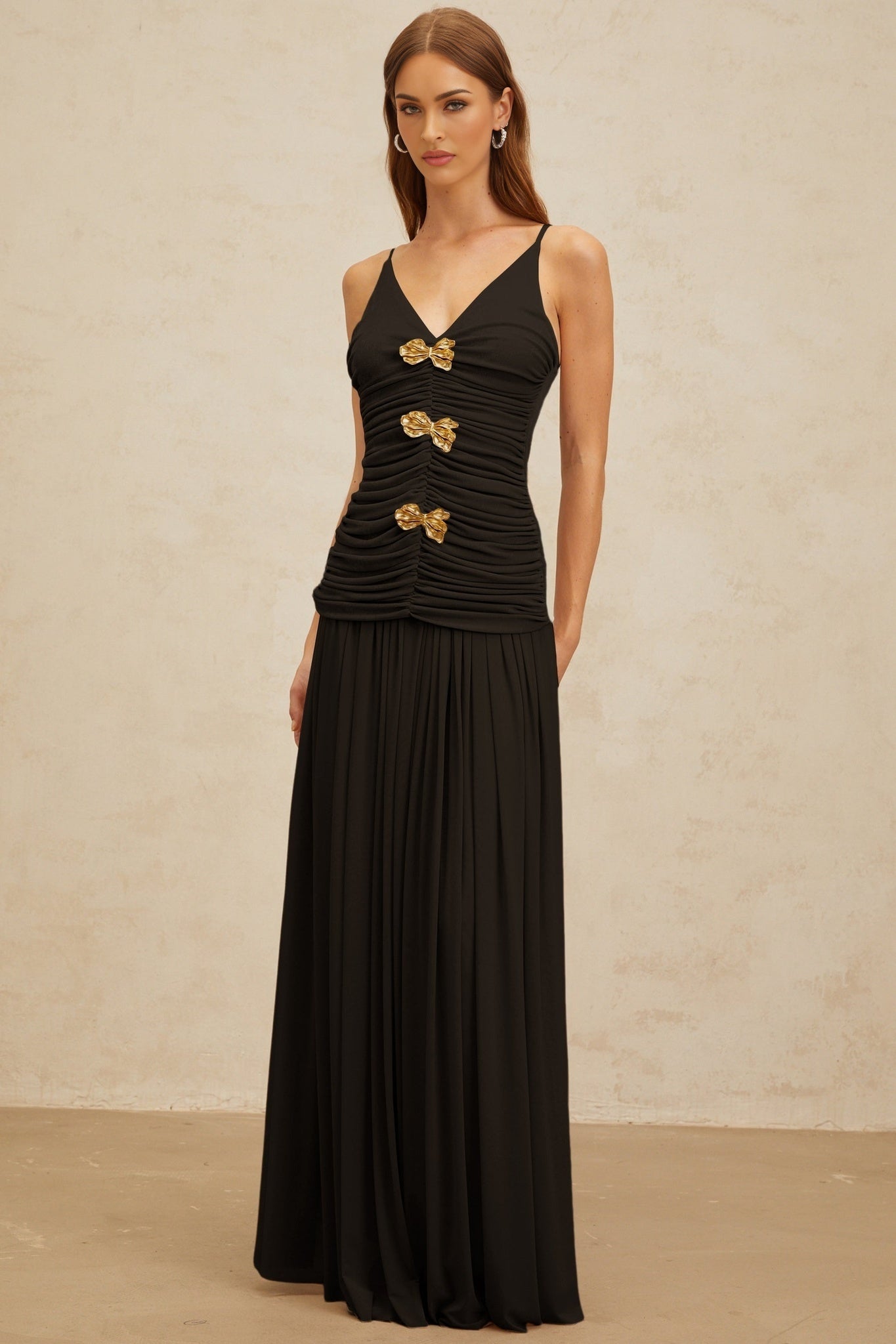 Black V-neck sleeveless top with brooch and ruched detailing, adjustable spaghetti straps, and rear zip fastening, paired with black pleated maxi skirt with rear zip fastening