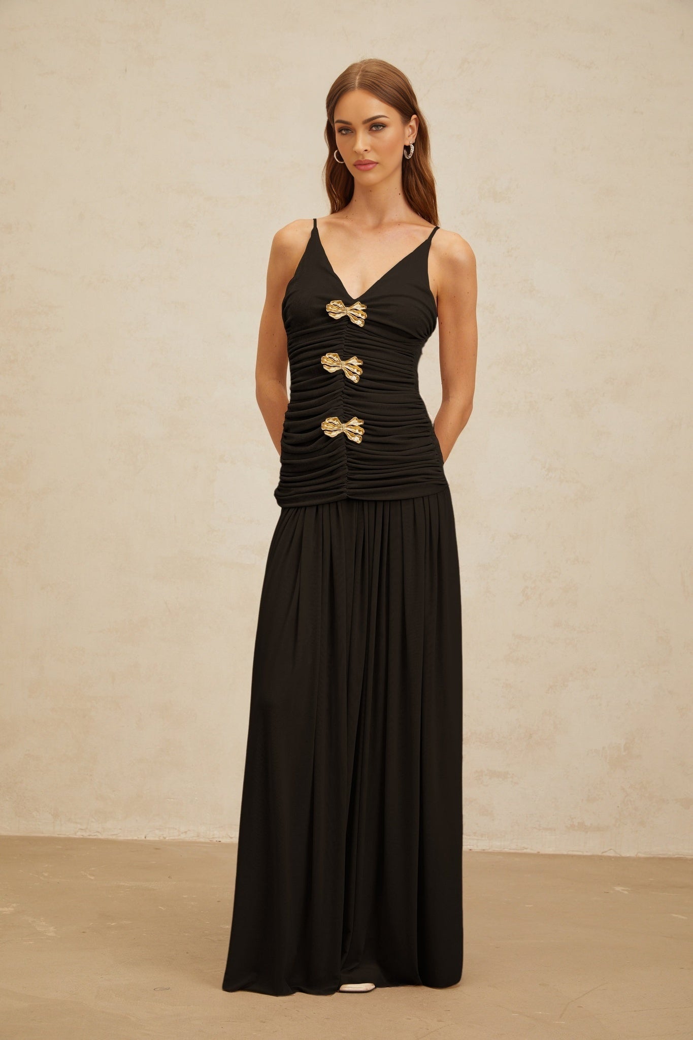 Black V-neck sleeveless top with brooch and ruched detailing, adjustable spaghetti straps, and rear zip fastening paired with pleated black maxi skirt with rear zip fastening