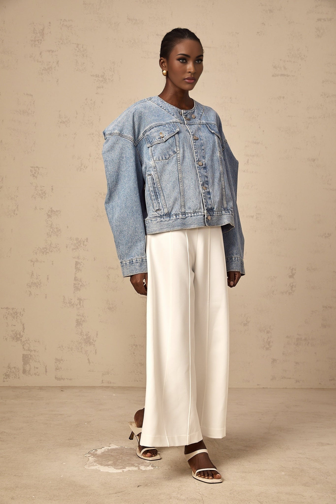 Blue collarless denim jacket worn by a woman standing against a plain background