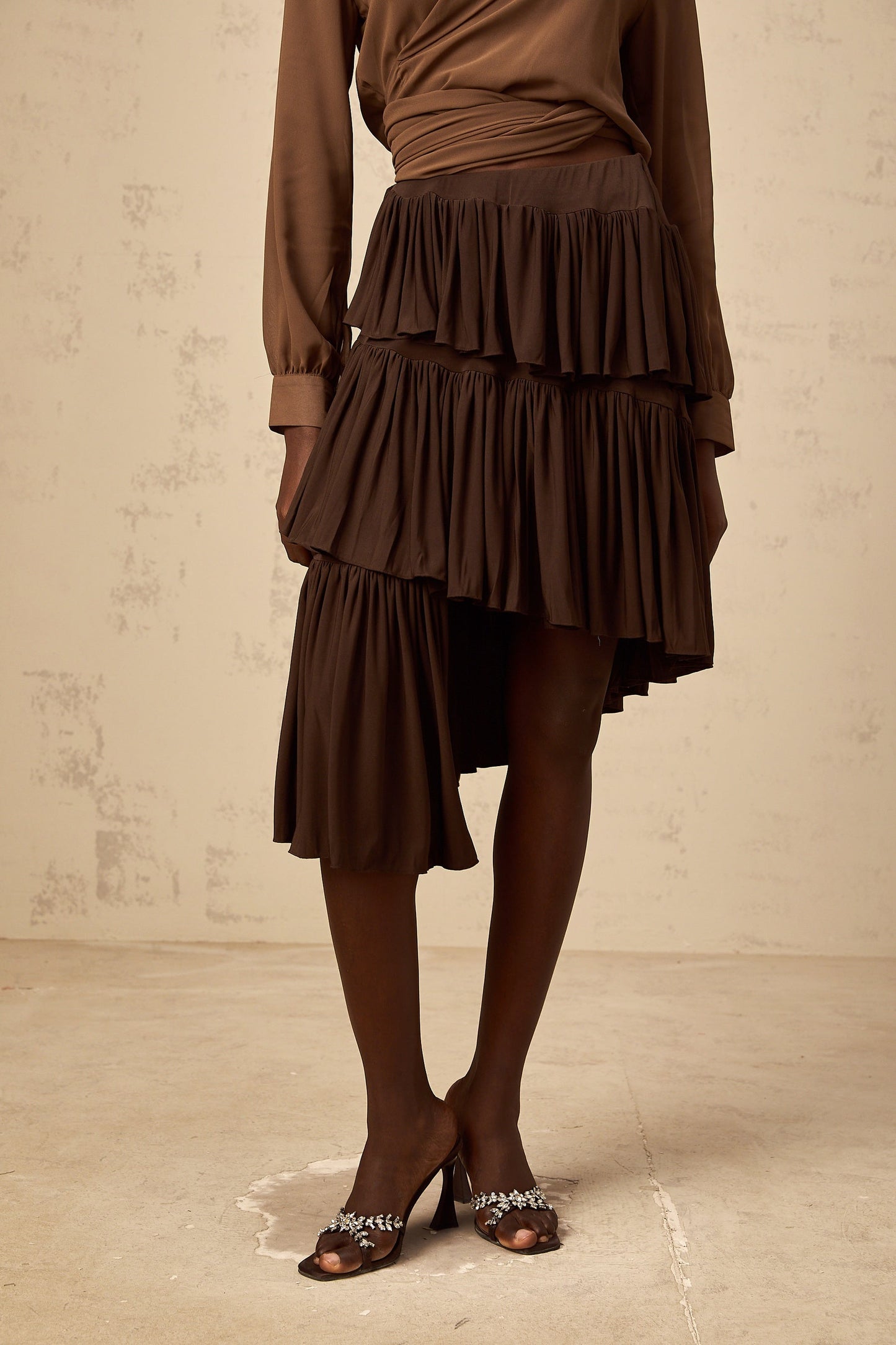 Brown asymmetrical mini skirt with pleated tiers and uneven hemline on white background