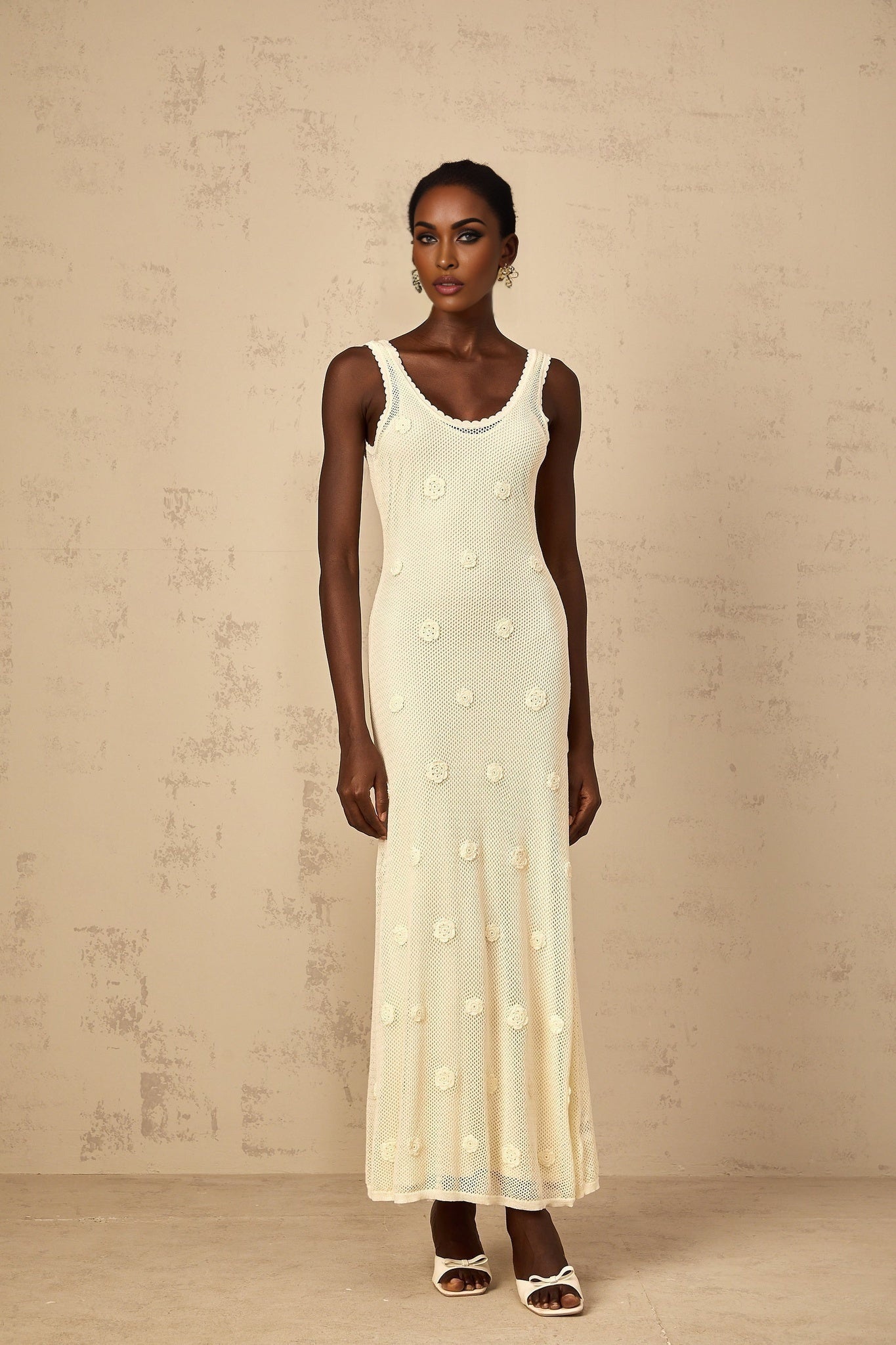 Elegant white maxi dress with floral embroidery and crochet knit details worn by a woman standing in a garden setting