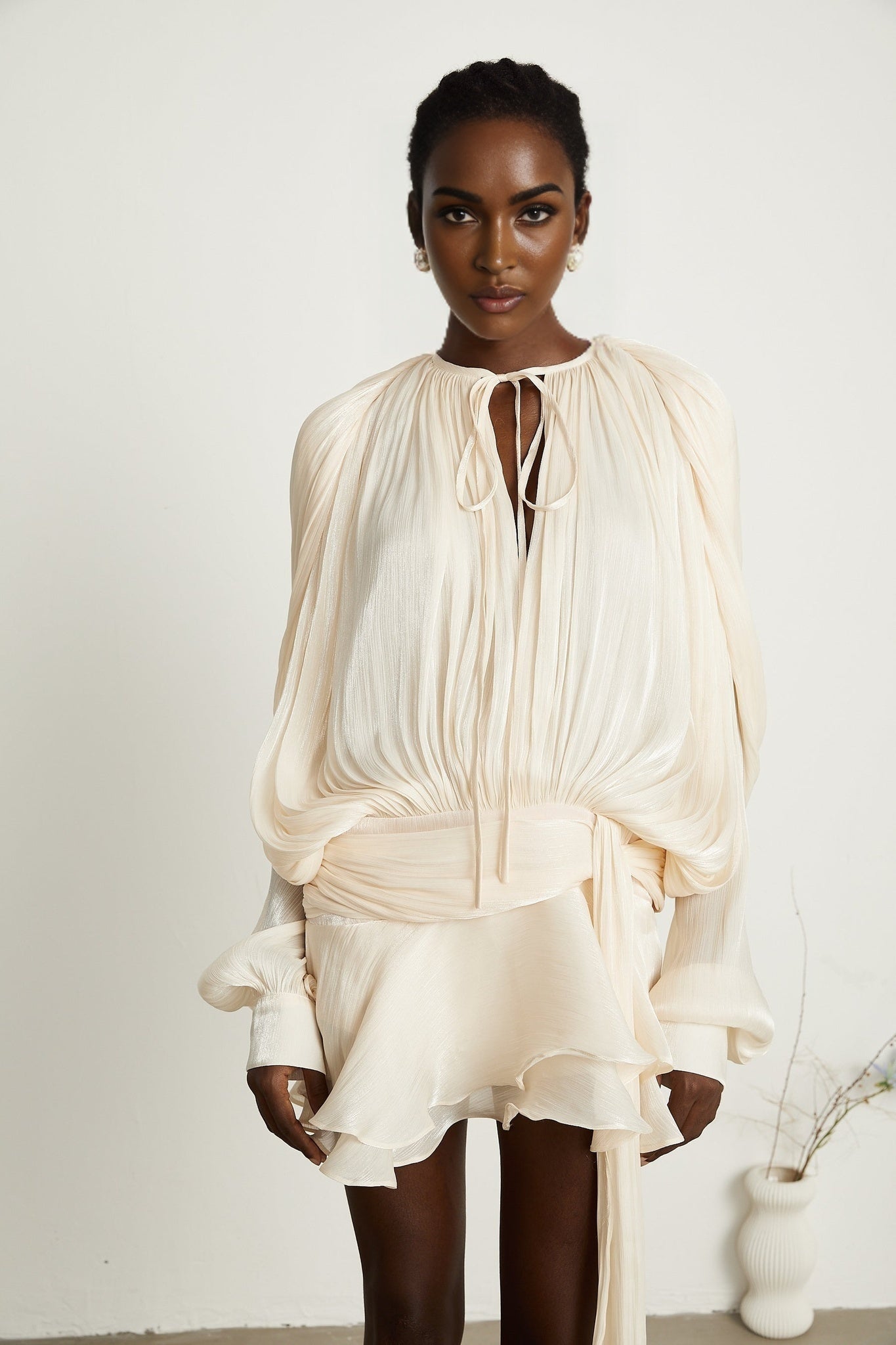 Eugenie fully pleated ruffled mini dress in neutral color standing on plain background