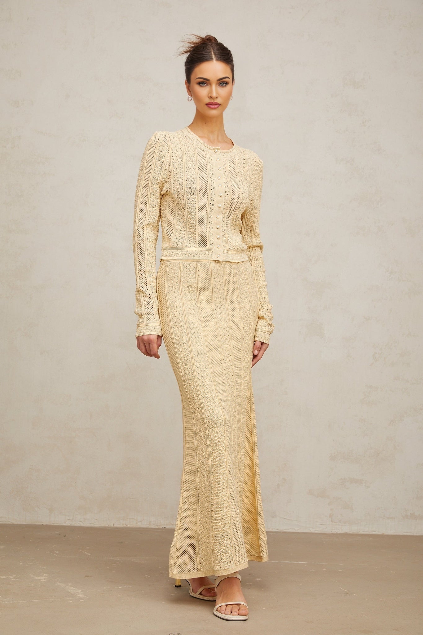 Matching set of a pointelle knit cardigan and skirt in light color worn by a model against a plain background