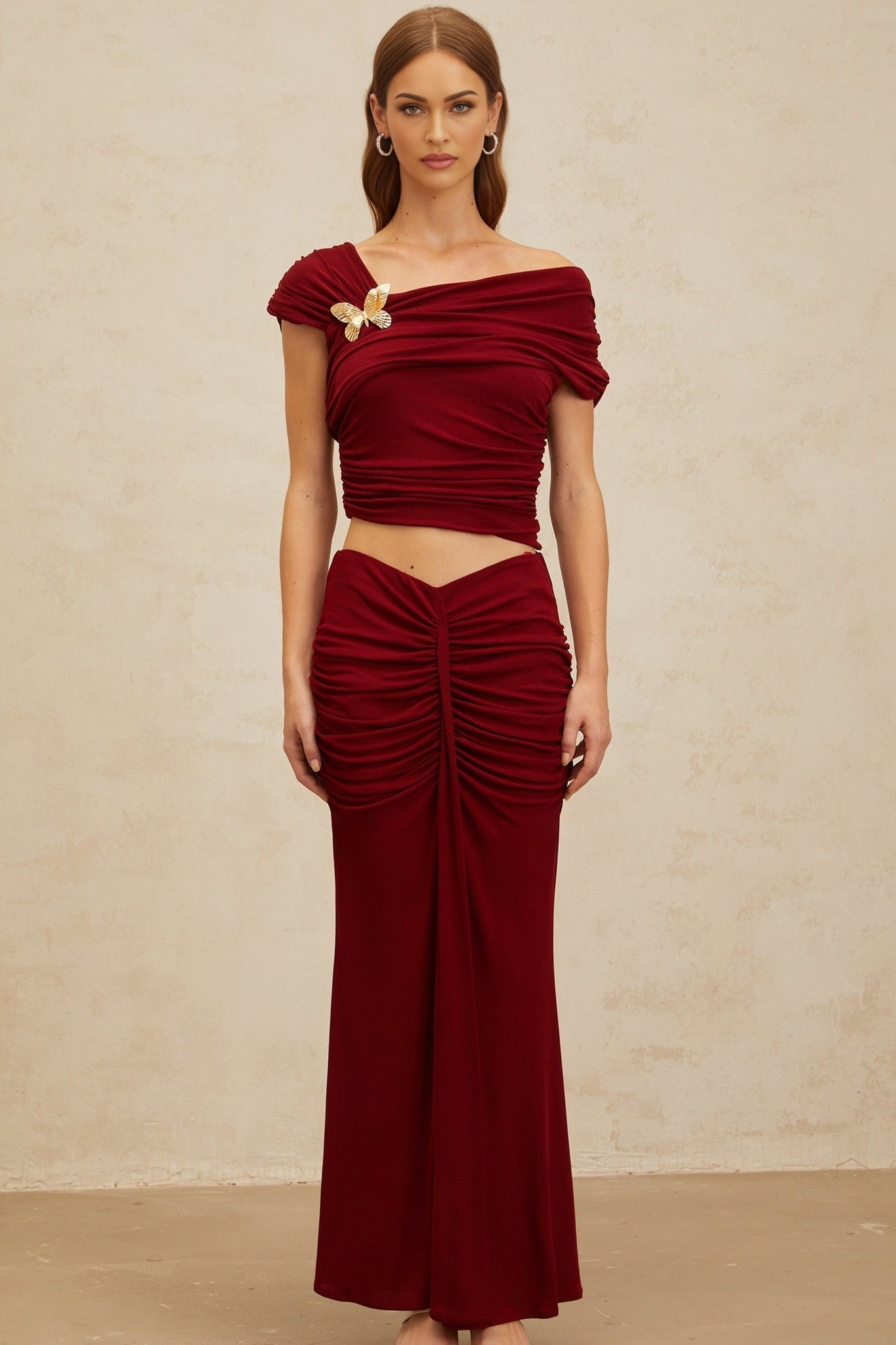 Red asymmetrical cropped top with butterfly brooch and cap sleeves, paired with red ruched mermaid hem maxi skirt