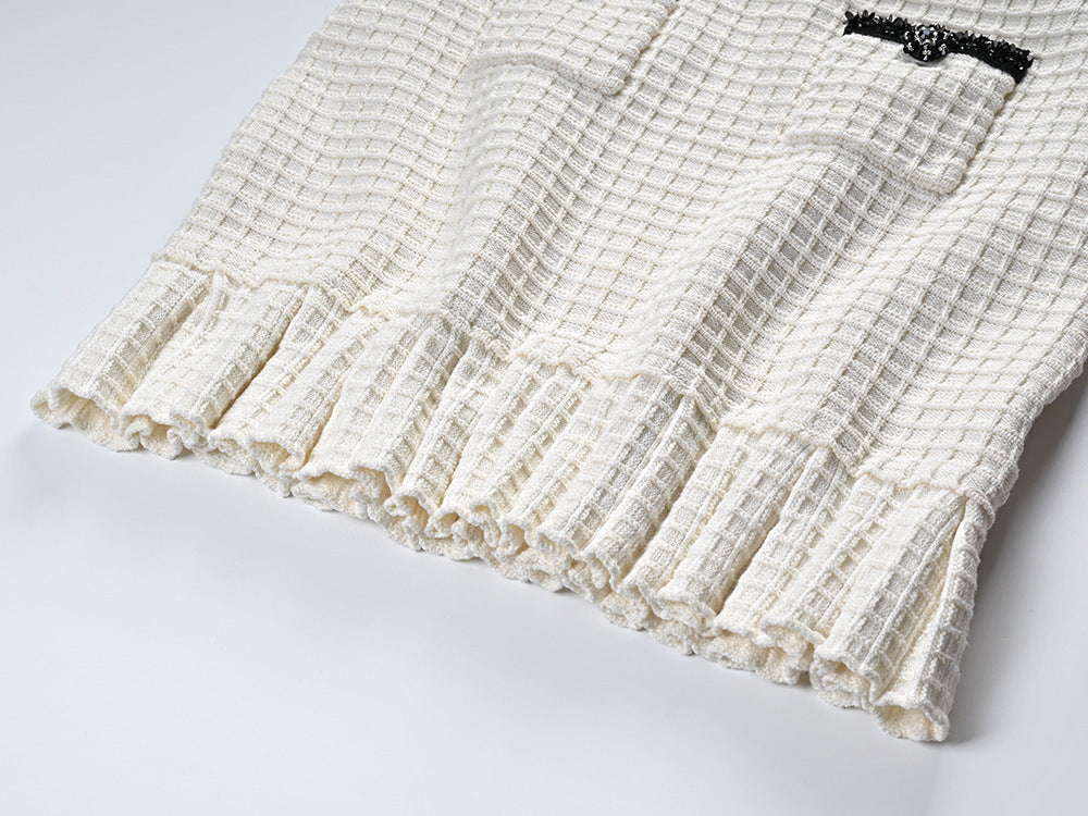 Textured white knitted jacket with black trim and decorative buttons paired with a ruffled hem skirt