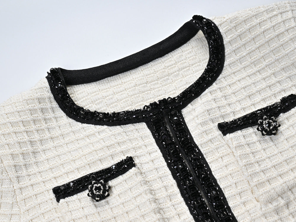 Textured white knitted jacket with black trim and decorative buttons paired with a ruffled hem skirt