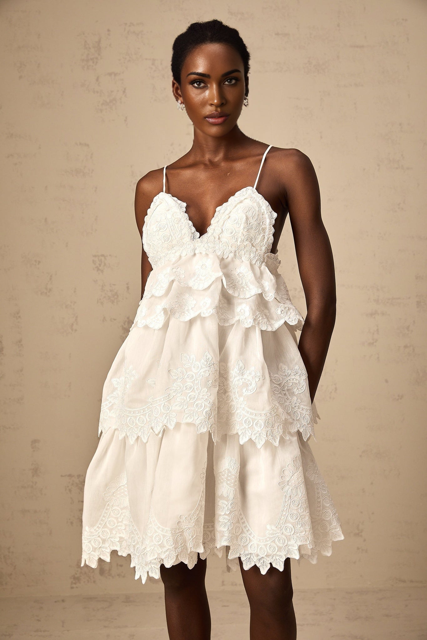 Valeria white mini dress with tiered skirt and guipure lace detailing shown on a model against a plain background