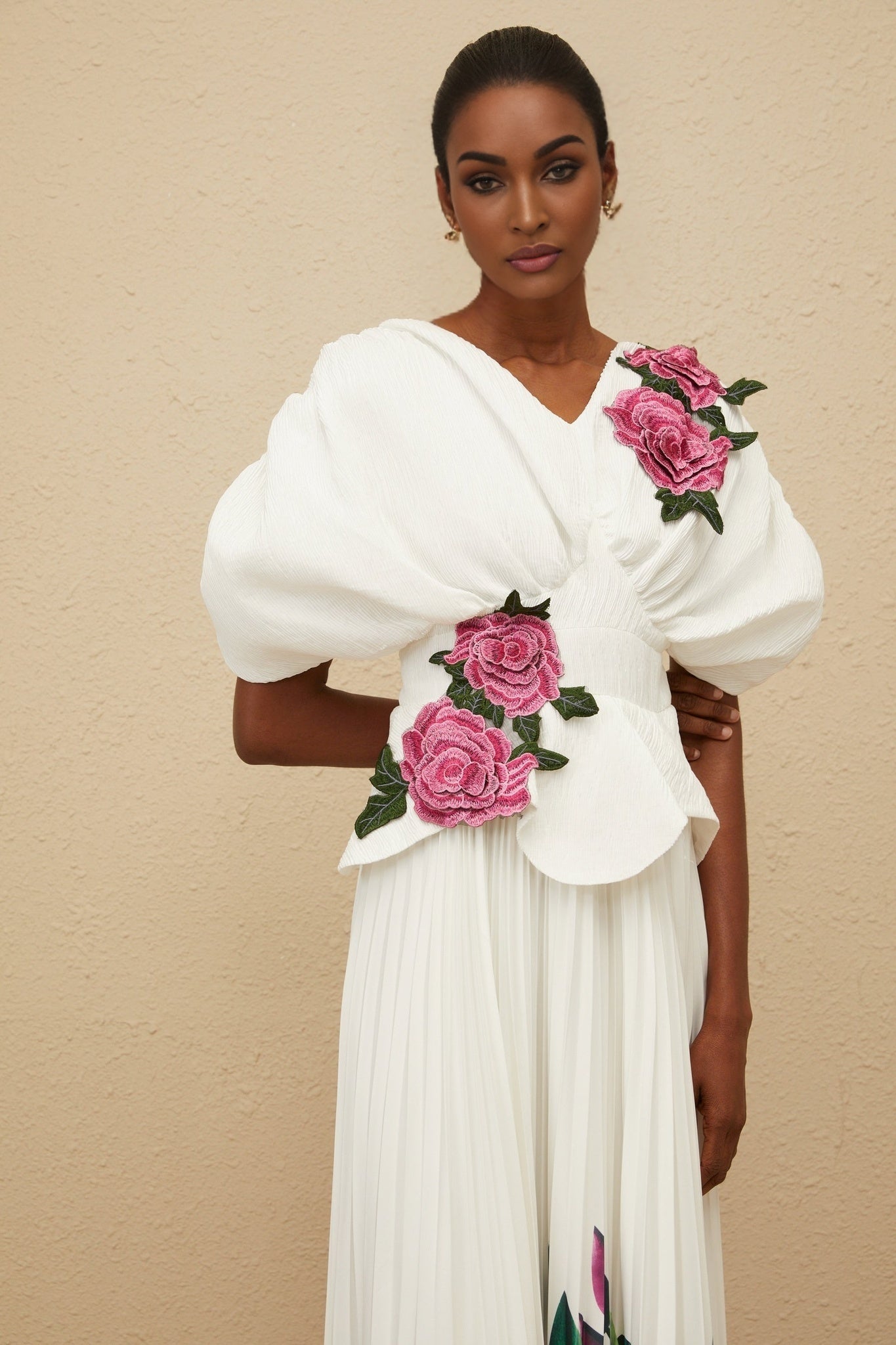 White V-neck batwing sleeve floral embroidered top with shirred effect and rear zip fastening, curved hem. White high rise pleated skirt with rose print, maxi length.