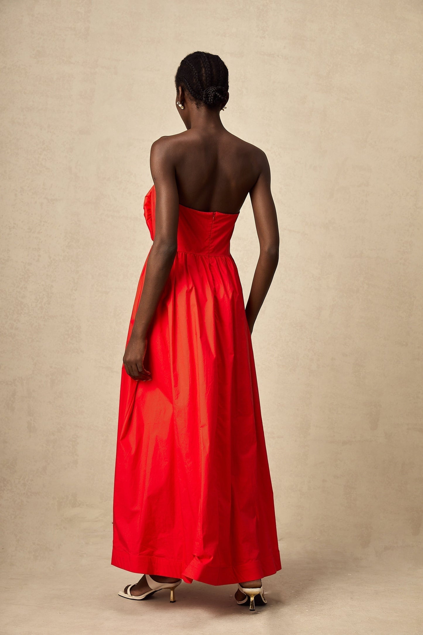 Woman in long red maxi dress with 3d ruffled petal details flowing from bodice to hem