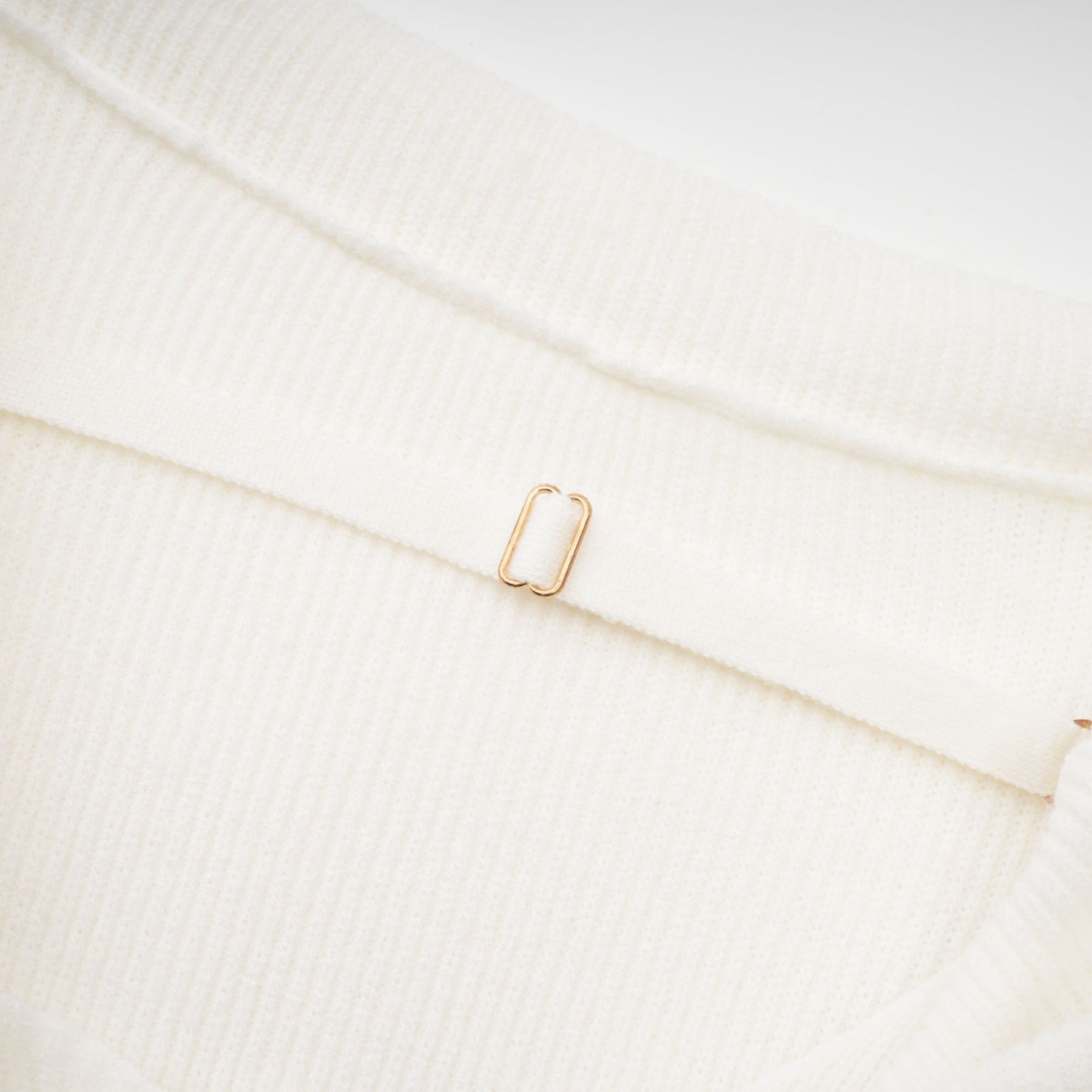 Woman wearing a beige knitted off shoulder long sleeve top with ribbed texture