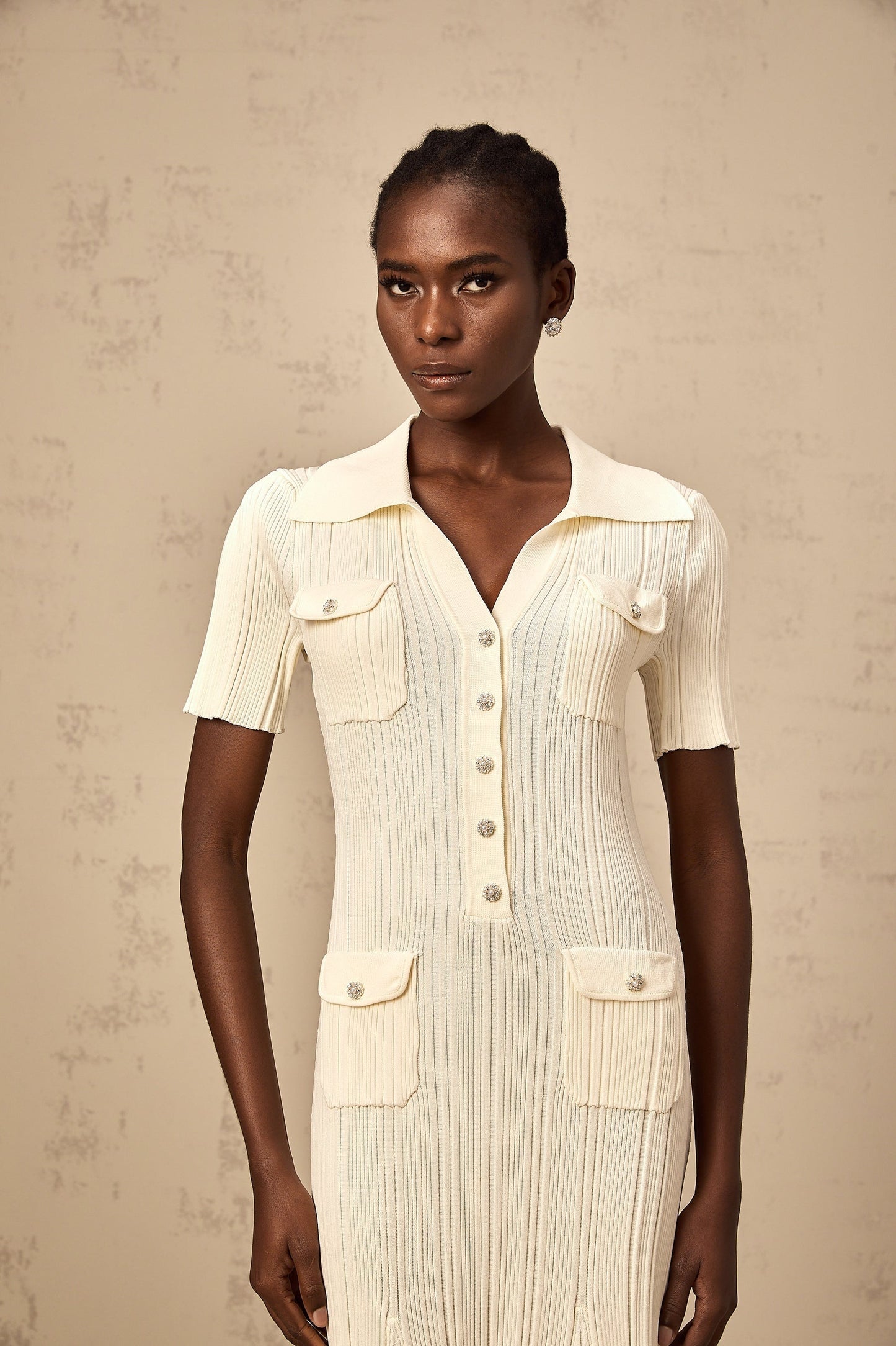 Woman wearing a beige ribbedknit midi dress with long sleeves and a fitted silhouette standing against a neutral background