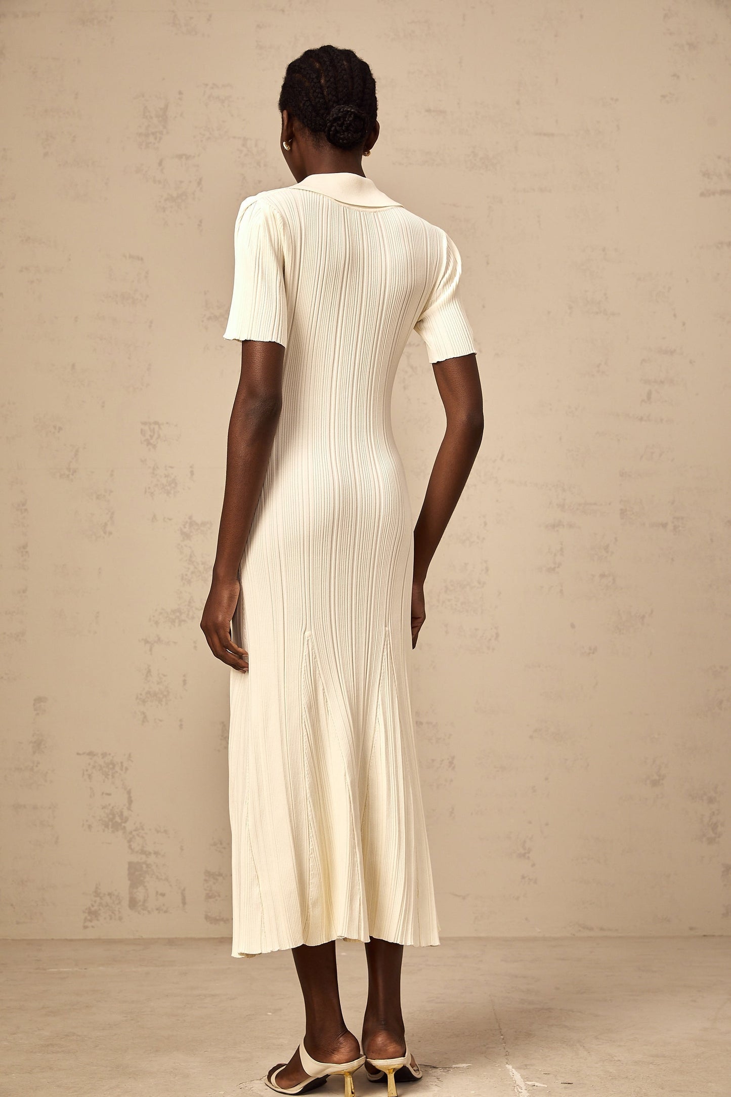Woman wearing a beige ribbedknit midi dress with long sleeves and a fitted silhouette standing against a plain background