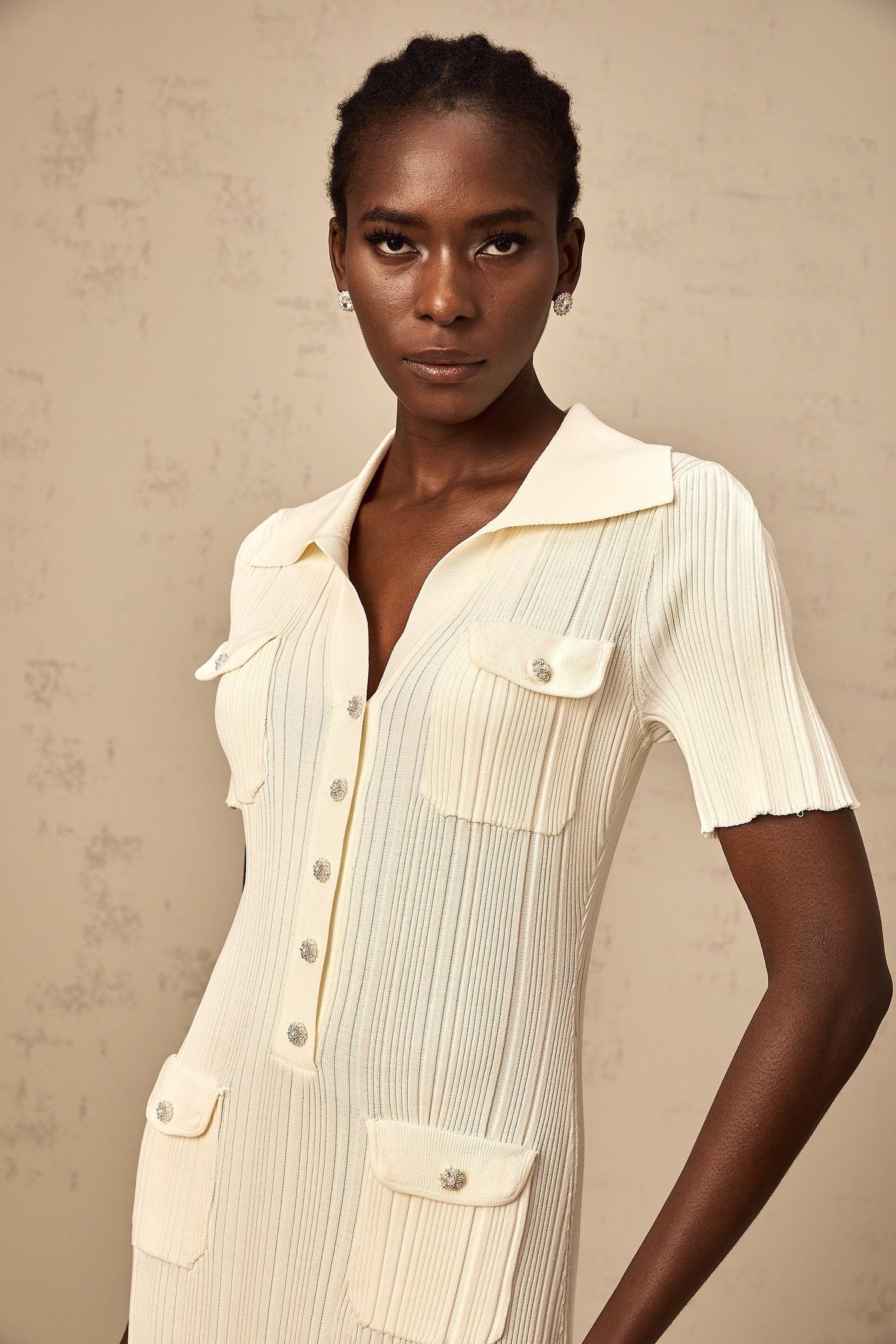 Woman wearing a beige ribbedknit midi dress with long sleeves and a formfitting silhouette standing against a plain background