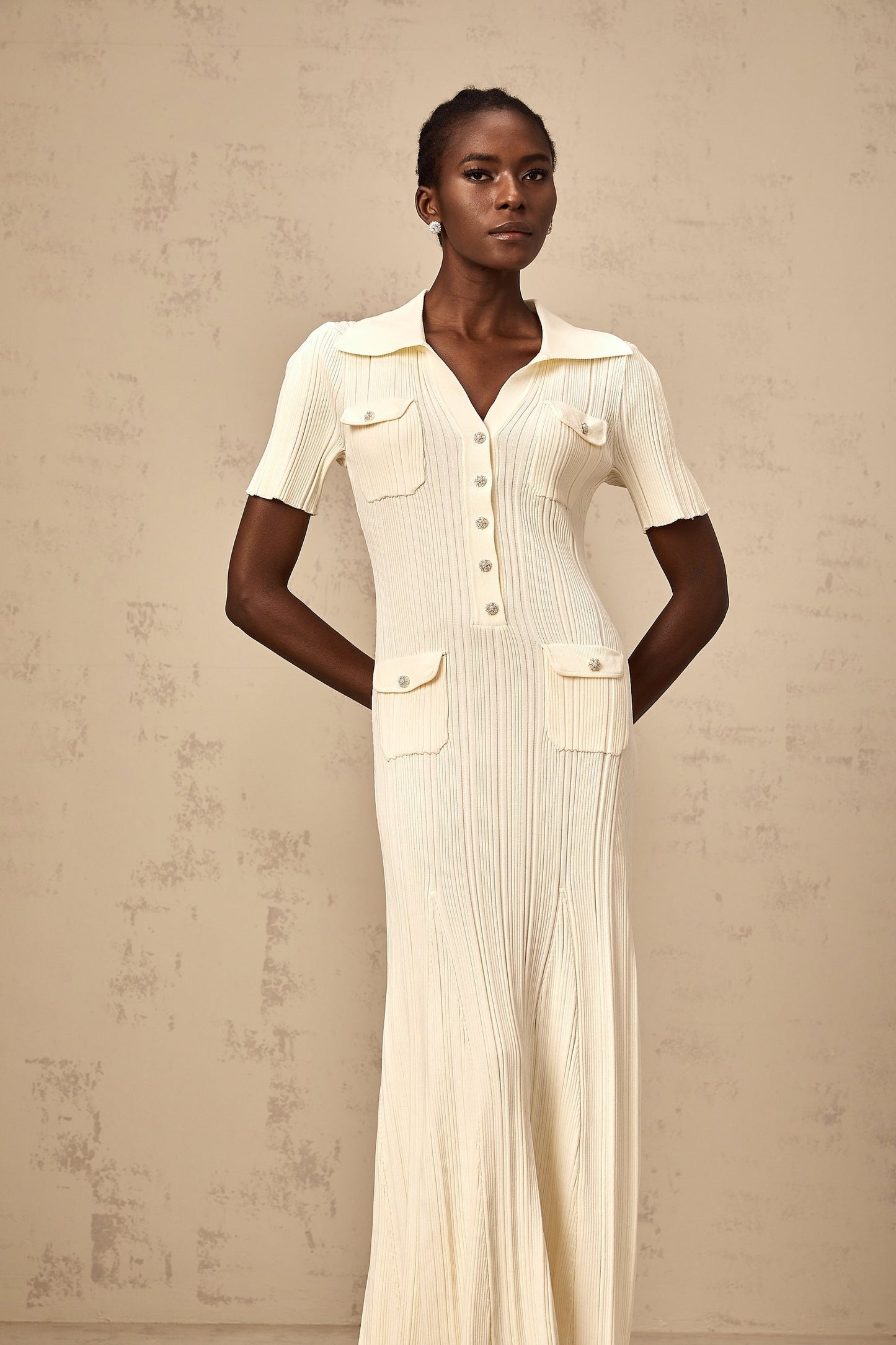 Woman wearing a beige ribbedknit midi dress with long sleeves and a formfitting silhouette standing against a plain background