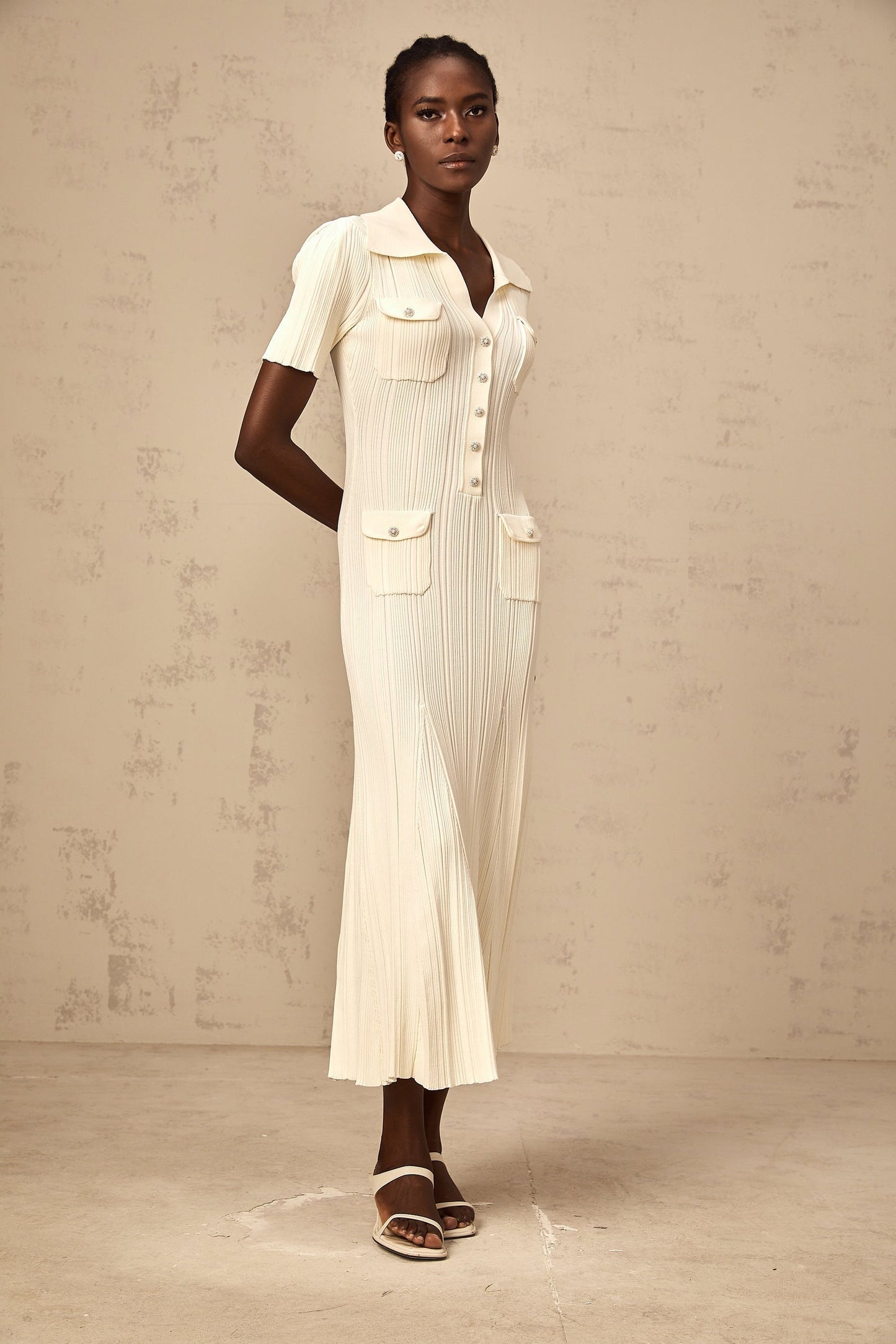 Woman wearing a beige ribbedknit midi dress with long sleeves and a formfitting silhouette standing against a plain background