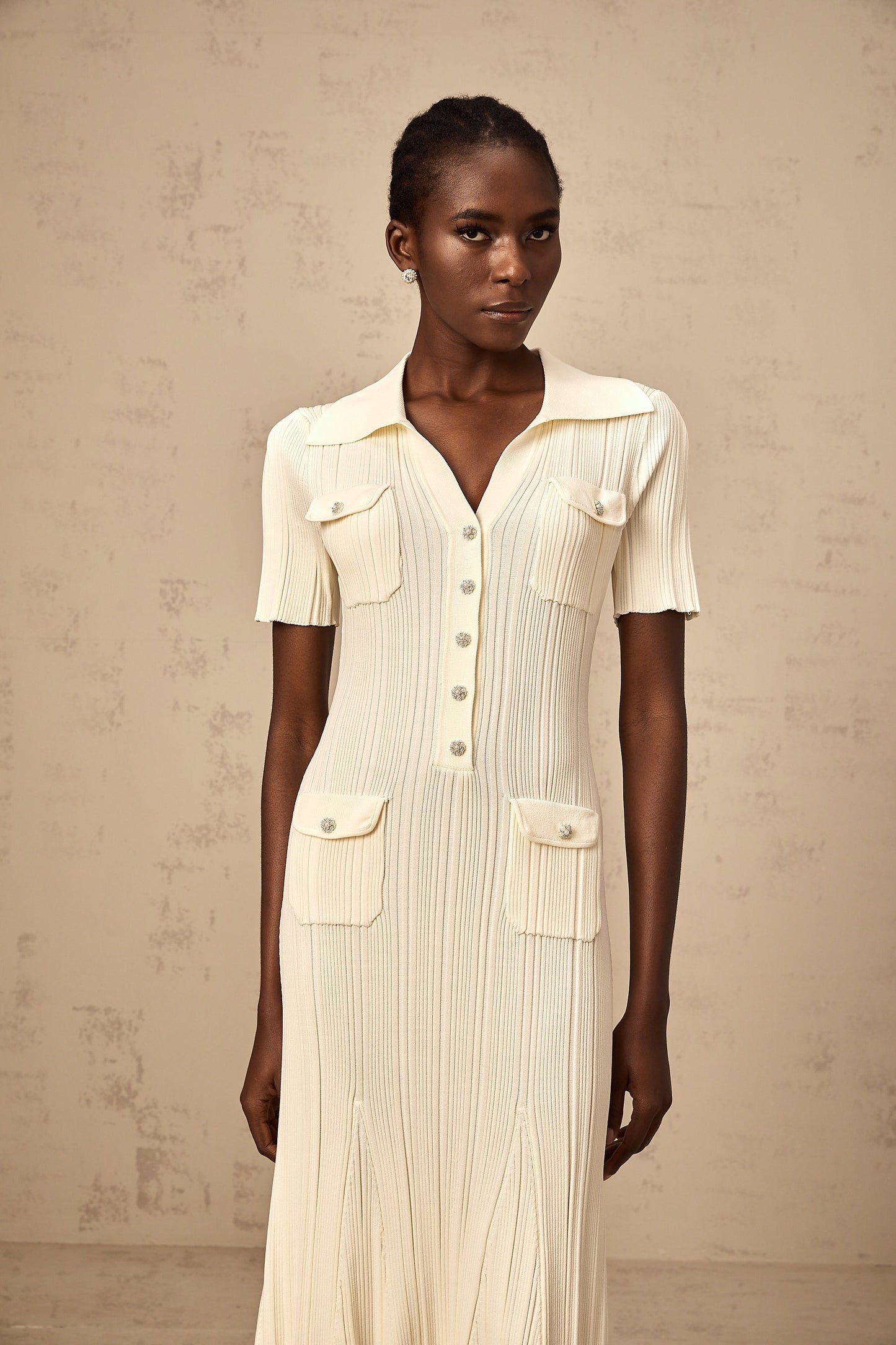 Woman wearing a beige ribbedknit midi dress with long sleeves and a formfitting silhouette standing in a neutral background