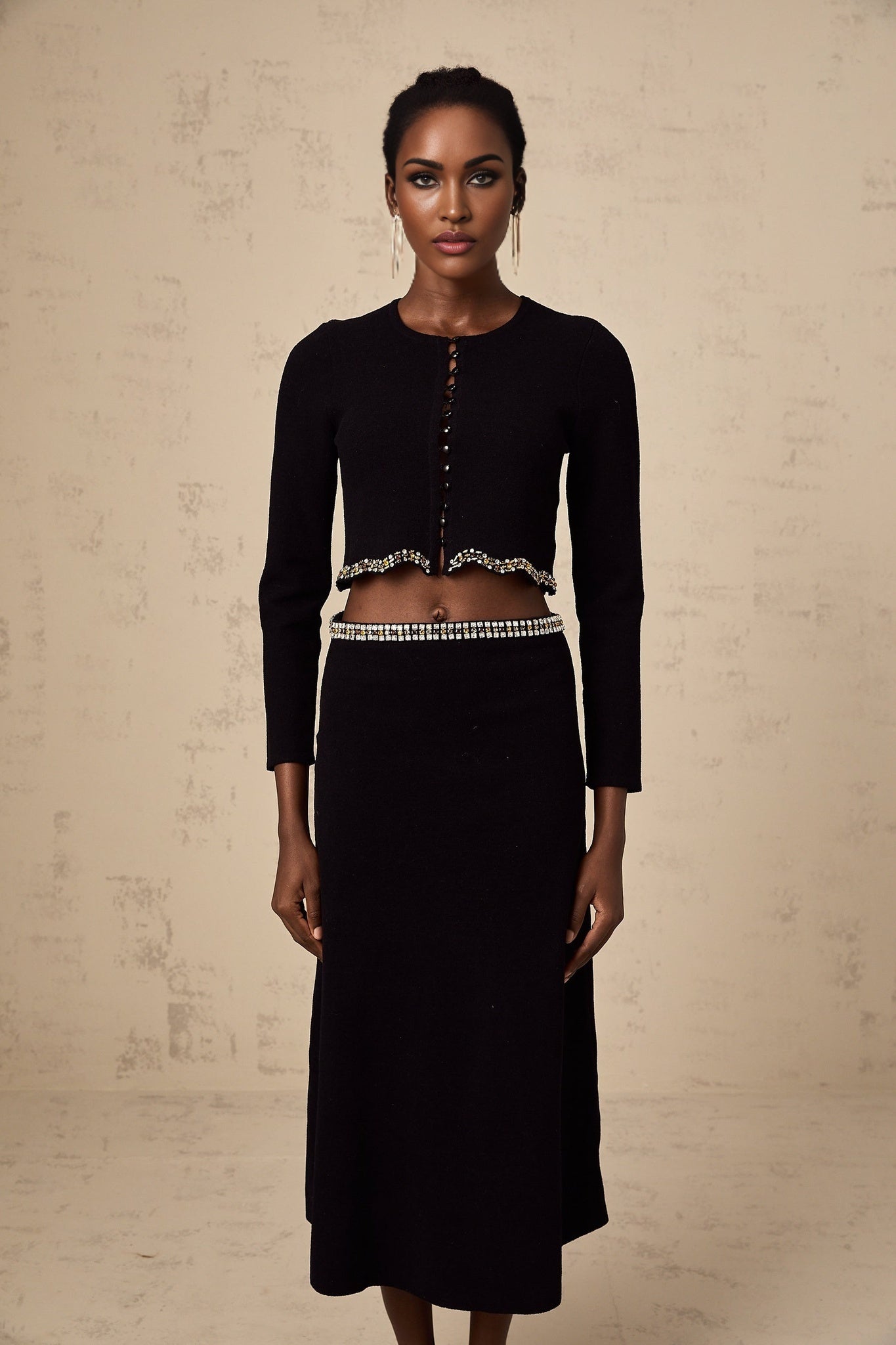 Woman wearing a black knitted cardigan and matching skirt set with embellishments named Magali