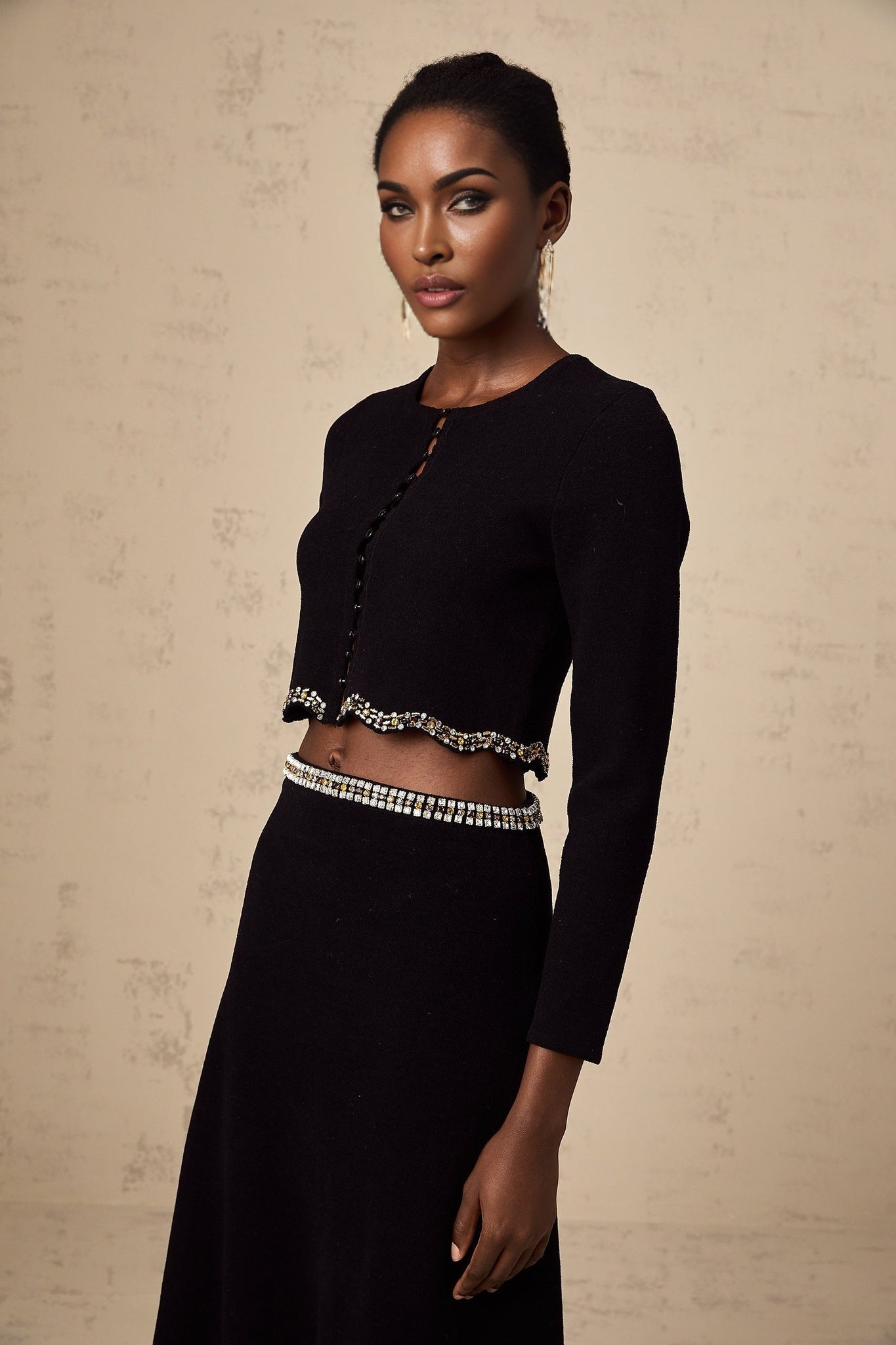 Woman wearing a black knitted cardigan and matching skirt set with embellishments named Magali