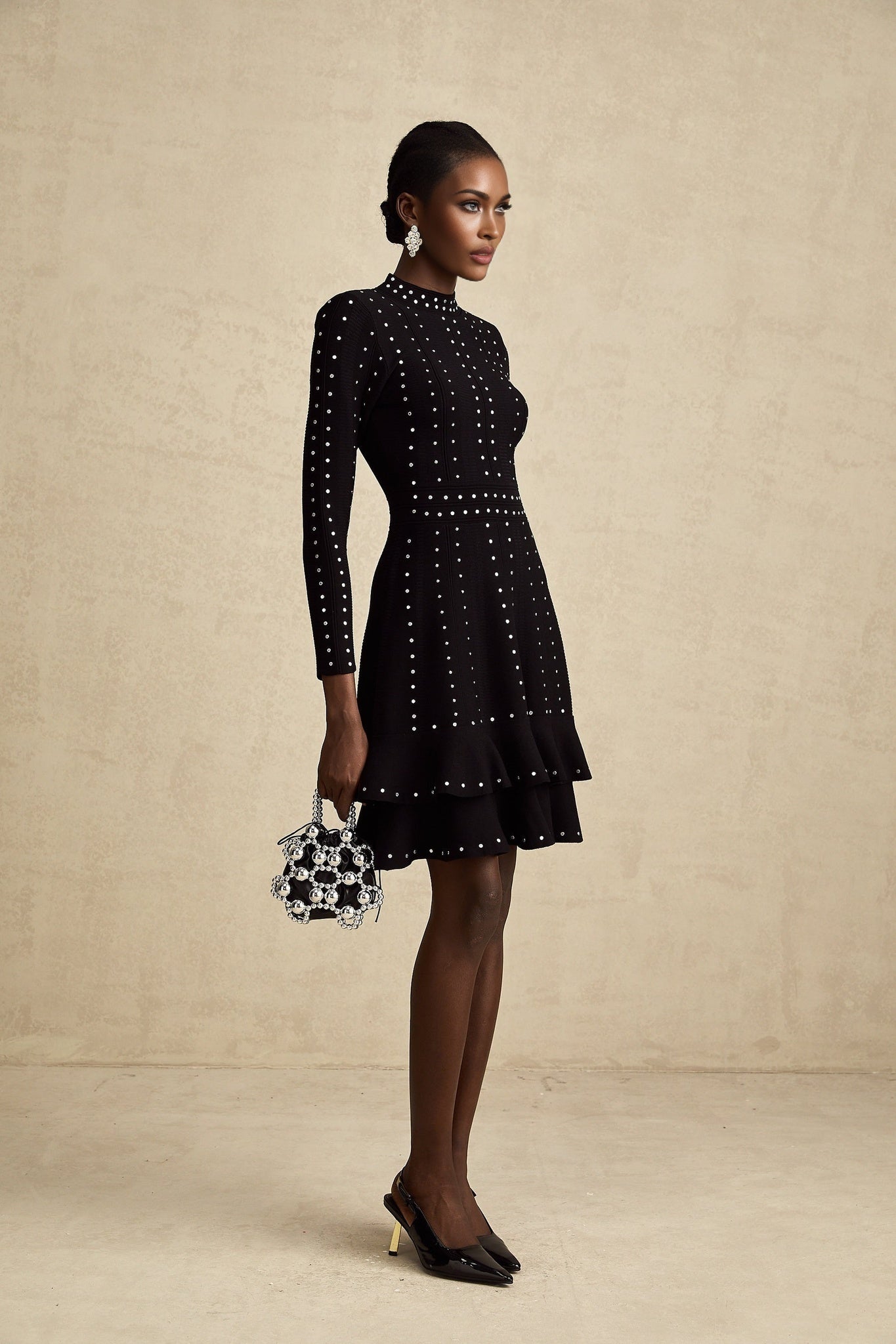 Woman wearing a black knitted mini dress with embellishments and ruffled details