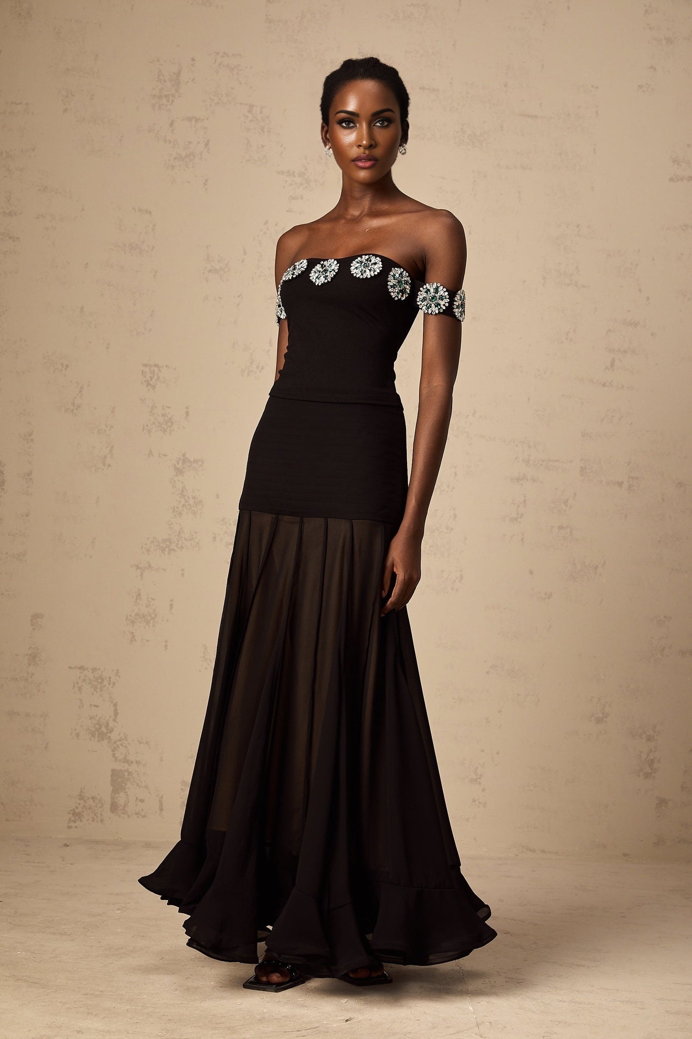 Woman wearing a black offshoulder top with embellishments named Carina