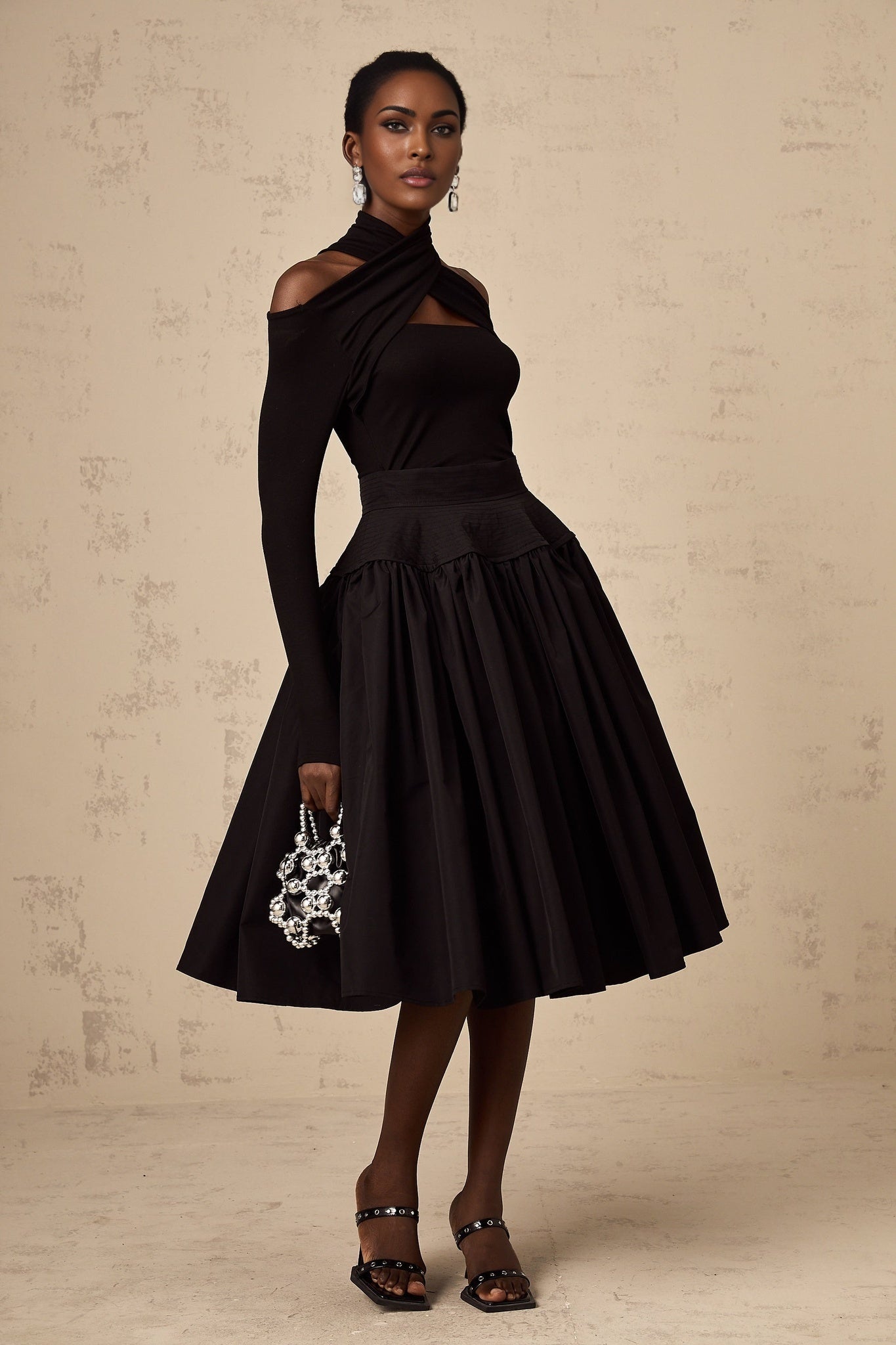 Woman wearing a black pleated midi skirt with flared silhouette standing against a plain background