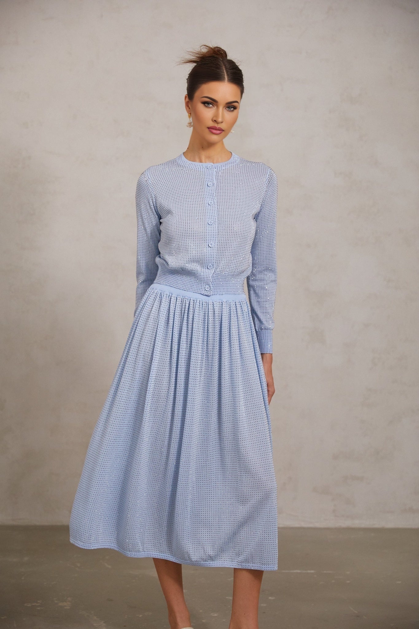 Woman wearing a blue knitted top and skirt set adorned with rhinestone details matching outfit with sparkly embellishments