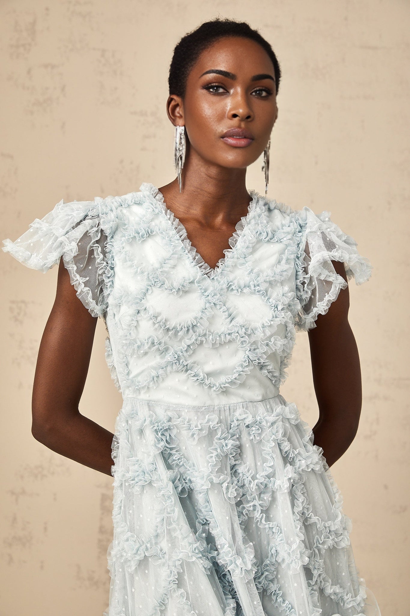 Woman wearing a blue midi dress with ruffled details and small white polka dots standing in a relaxed pose