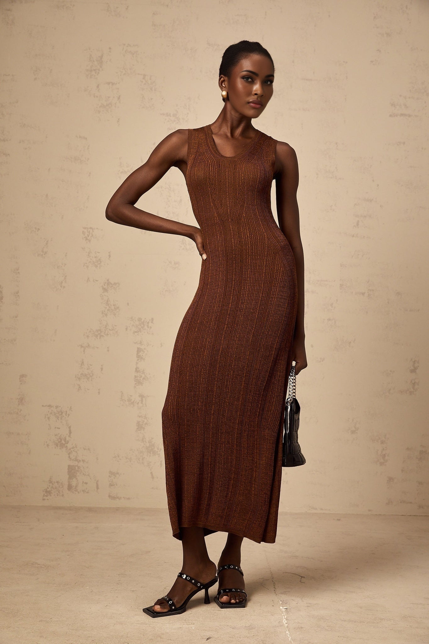 Woman wearing a brown knitted midi dress with cut out details standing in a neutral background