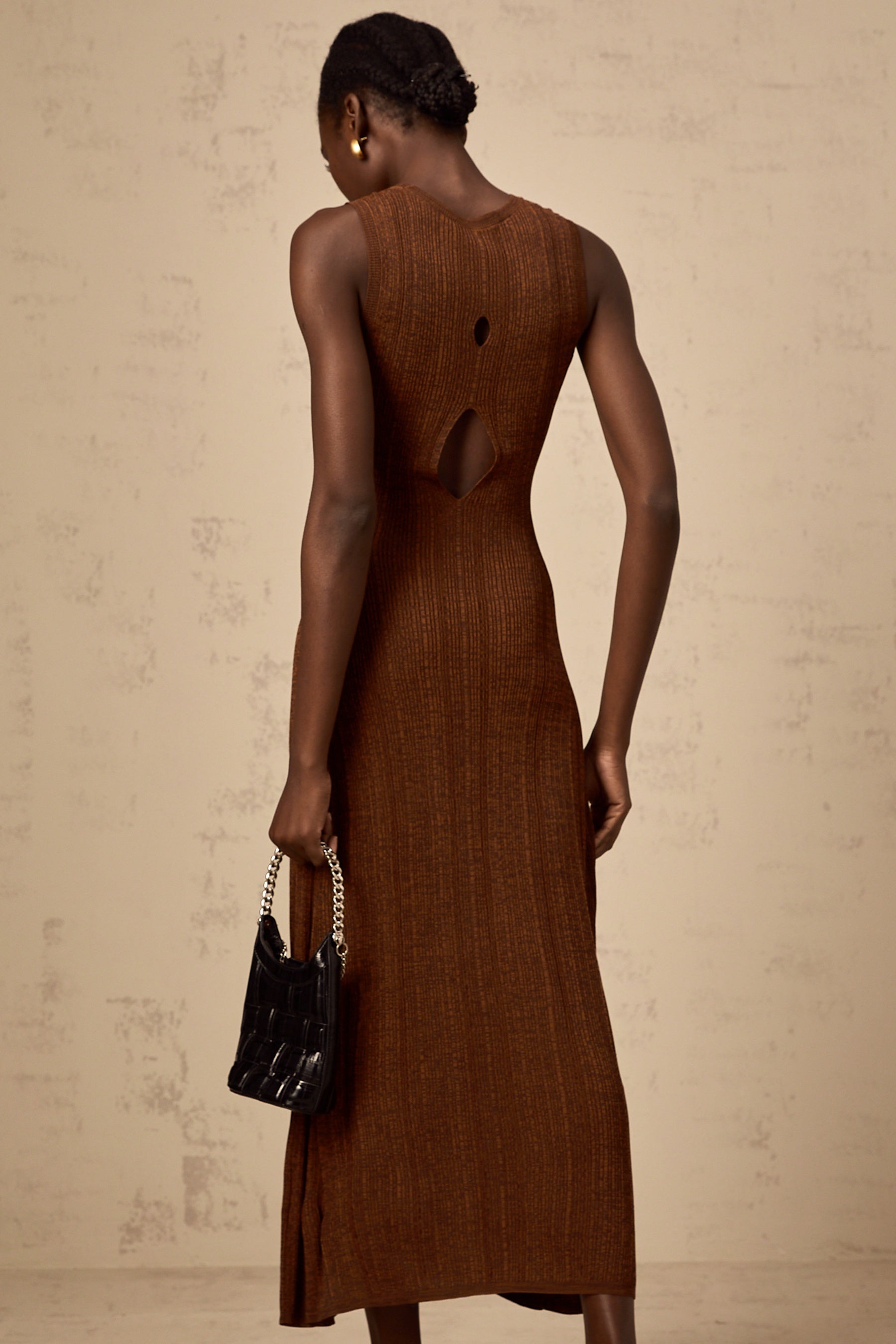 Woman wearing a brown knitted midi dress with cutout details standing in a neutral background