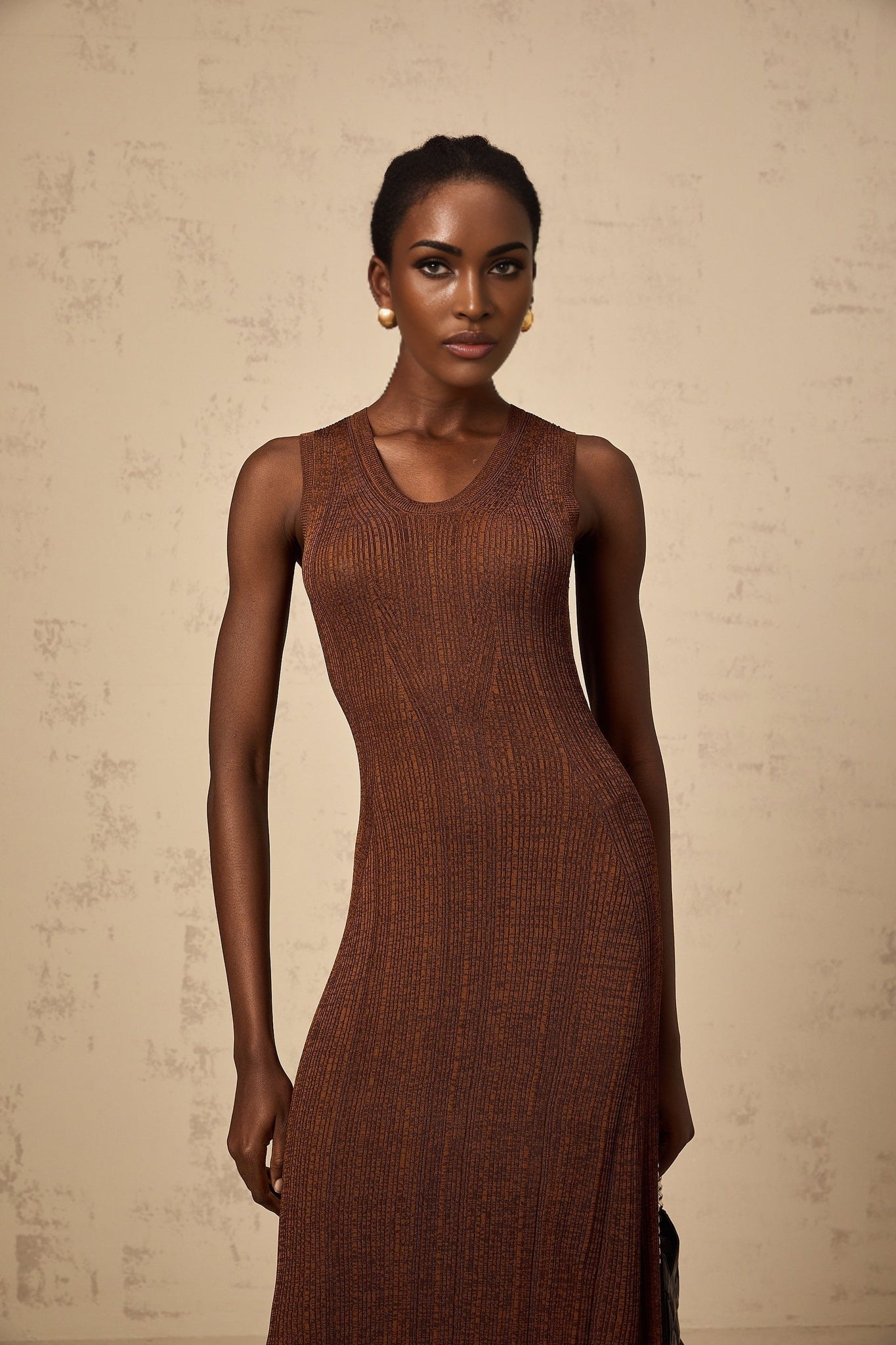 Woman wearing a brown knitted midi dress with cutout details standing in front of a plain background