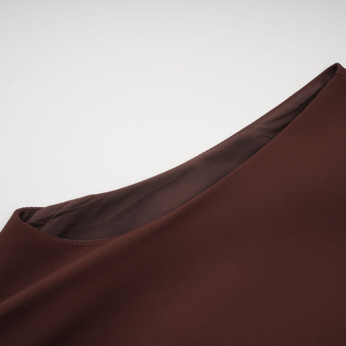 Woman wearing a brown mini dress with an asymmetric neckline and puffed sleeves standing against a plain background