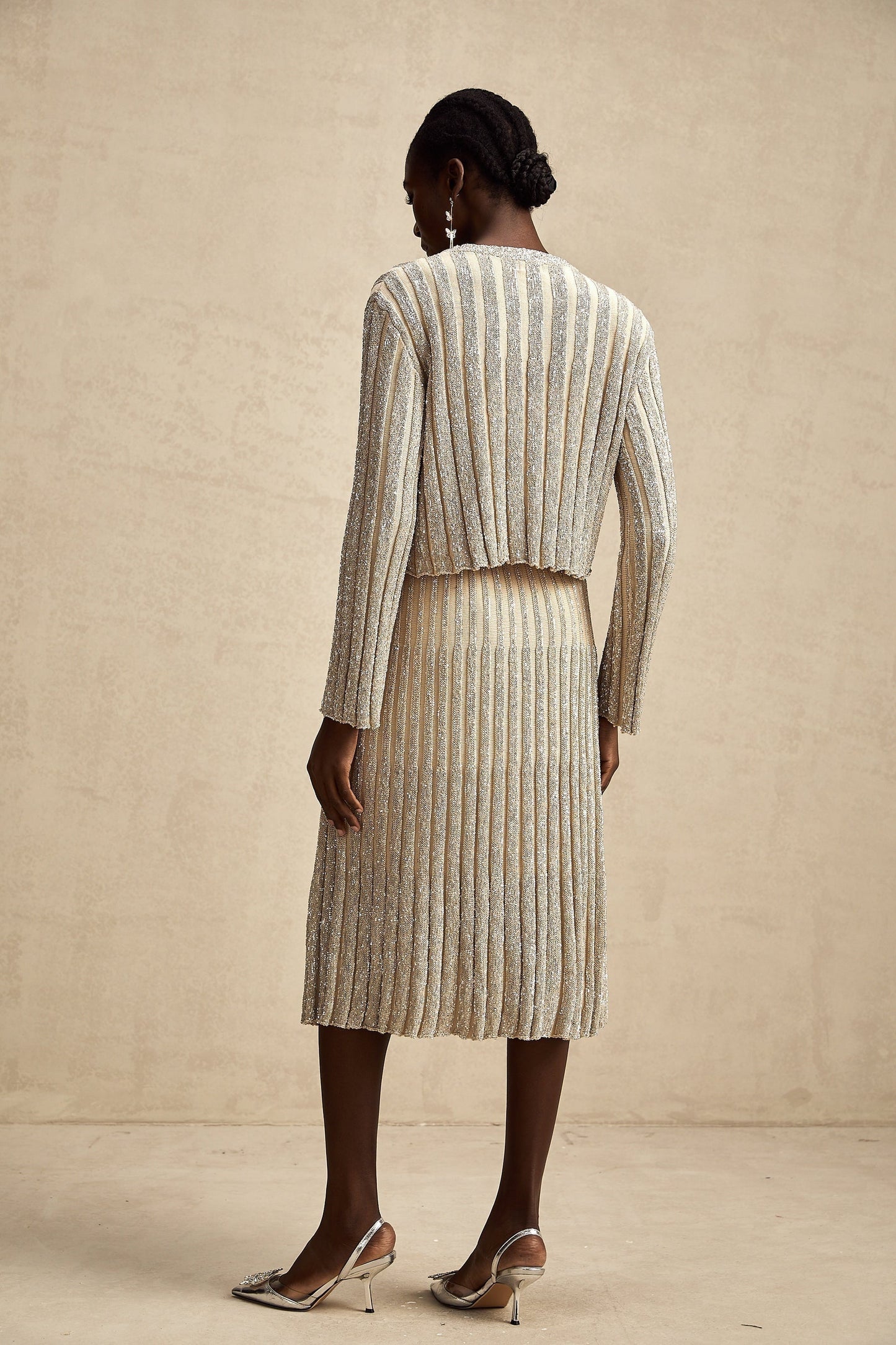 Woman wearing a champagne colored knit top and matching skirt with vertical stripes standing in a relaxed pose