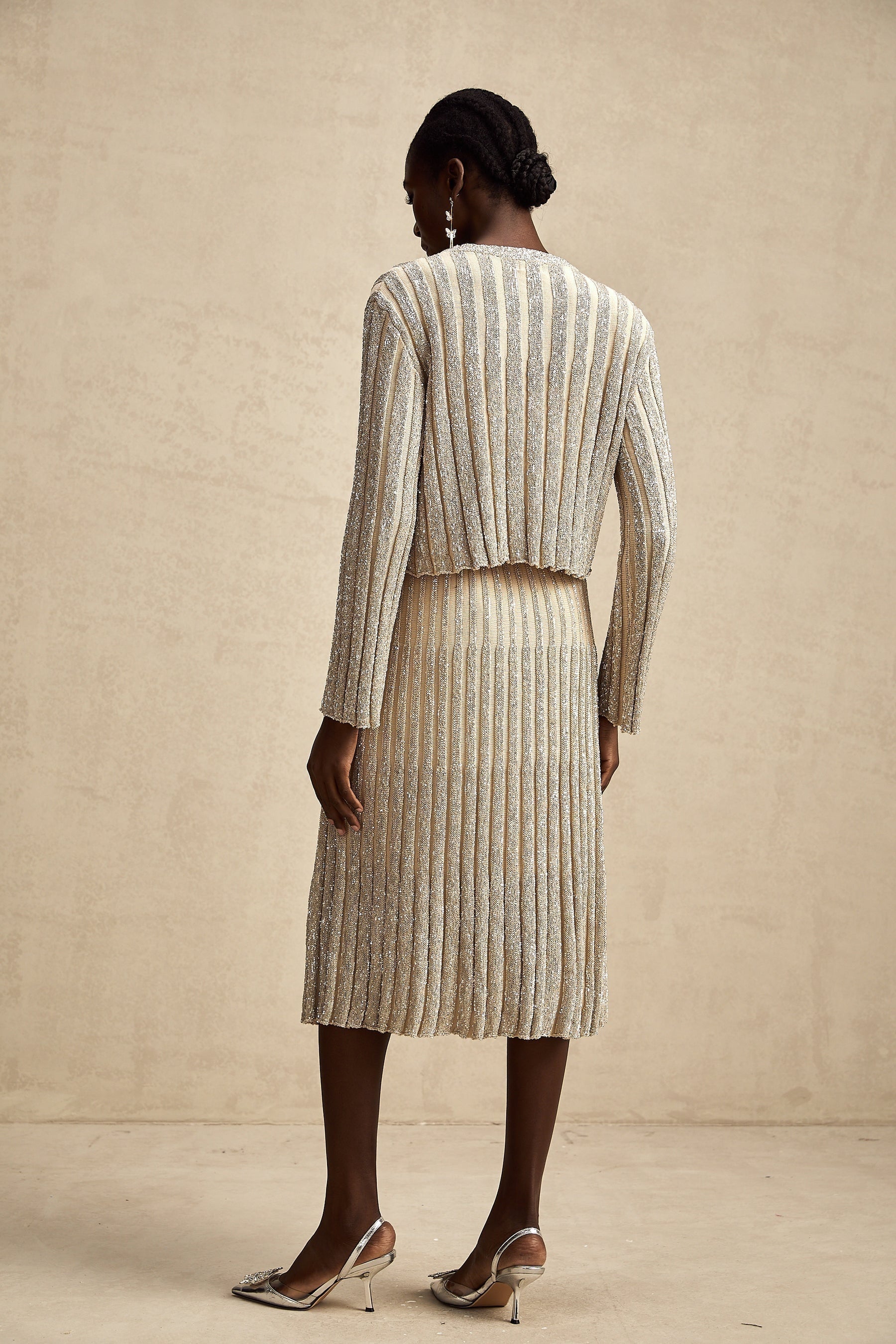 Woman wearing a champagne colored knit top and matching skirt with vertical stripes standing in a relaxed pose