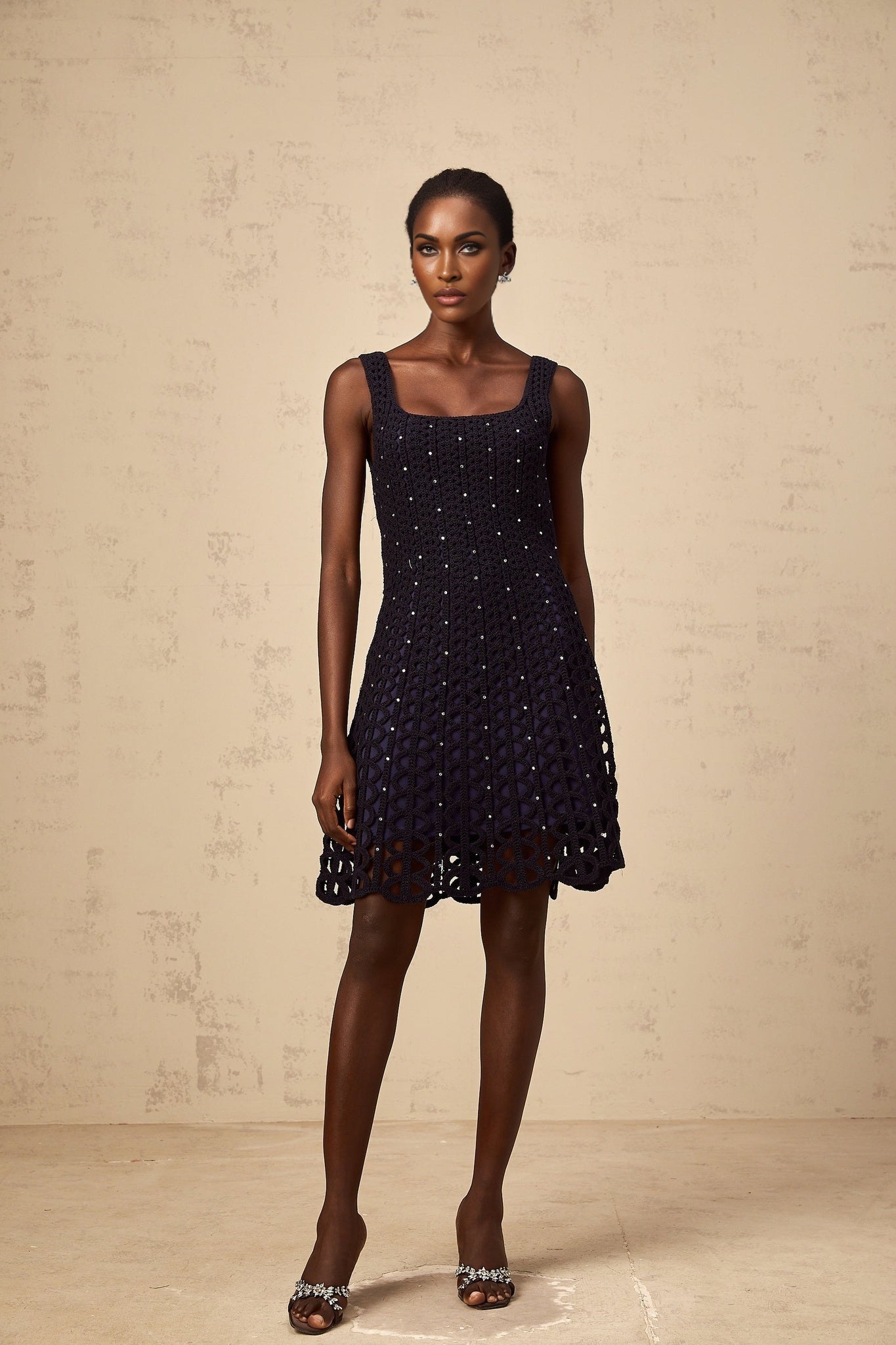 Woman wearing a dark blue mini dress with embellishments and crochet cutout details