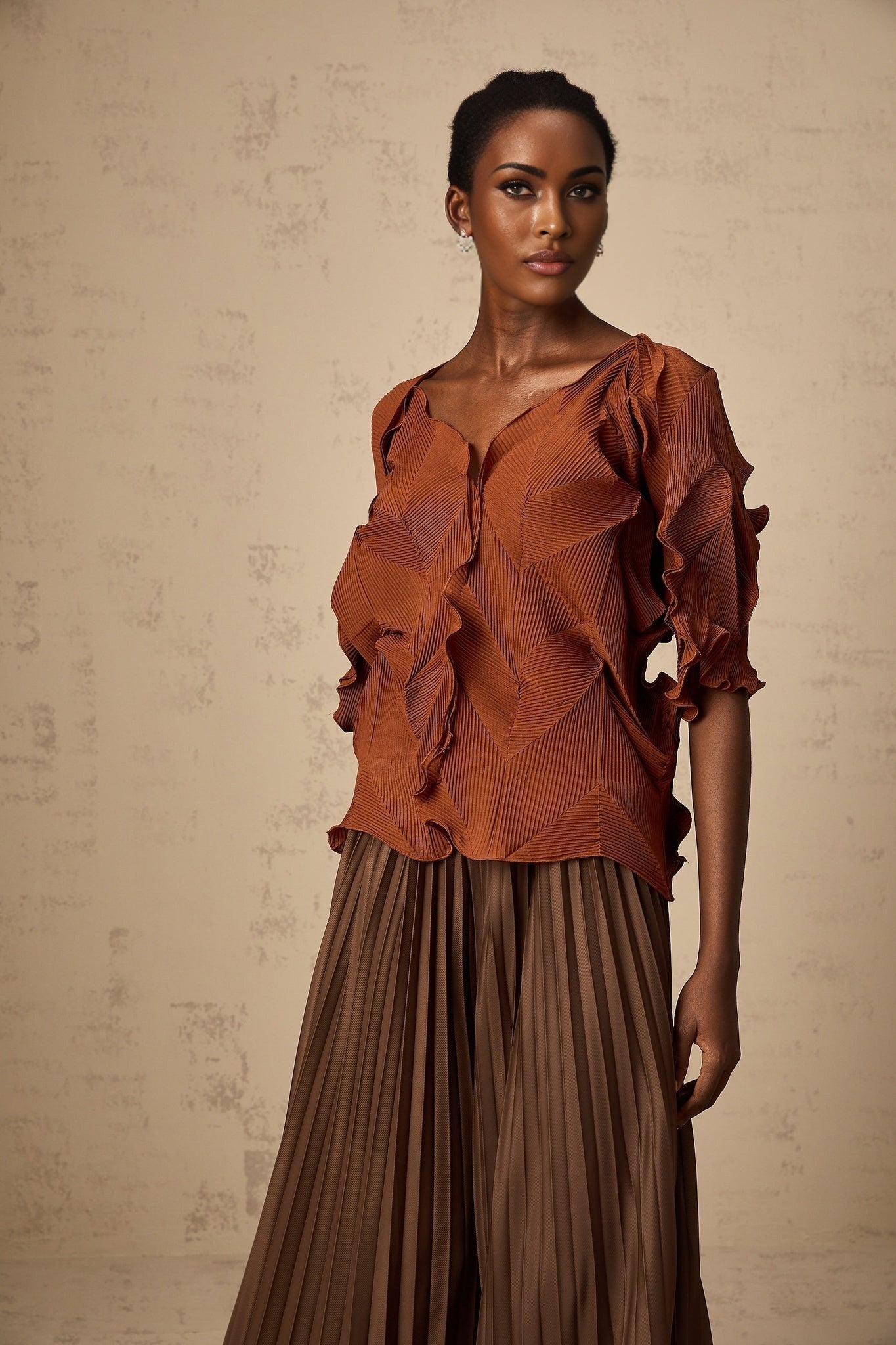 Woman wearing a demi brown matching set with creased texture top and skirt standing against plain background