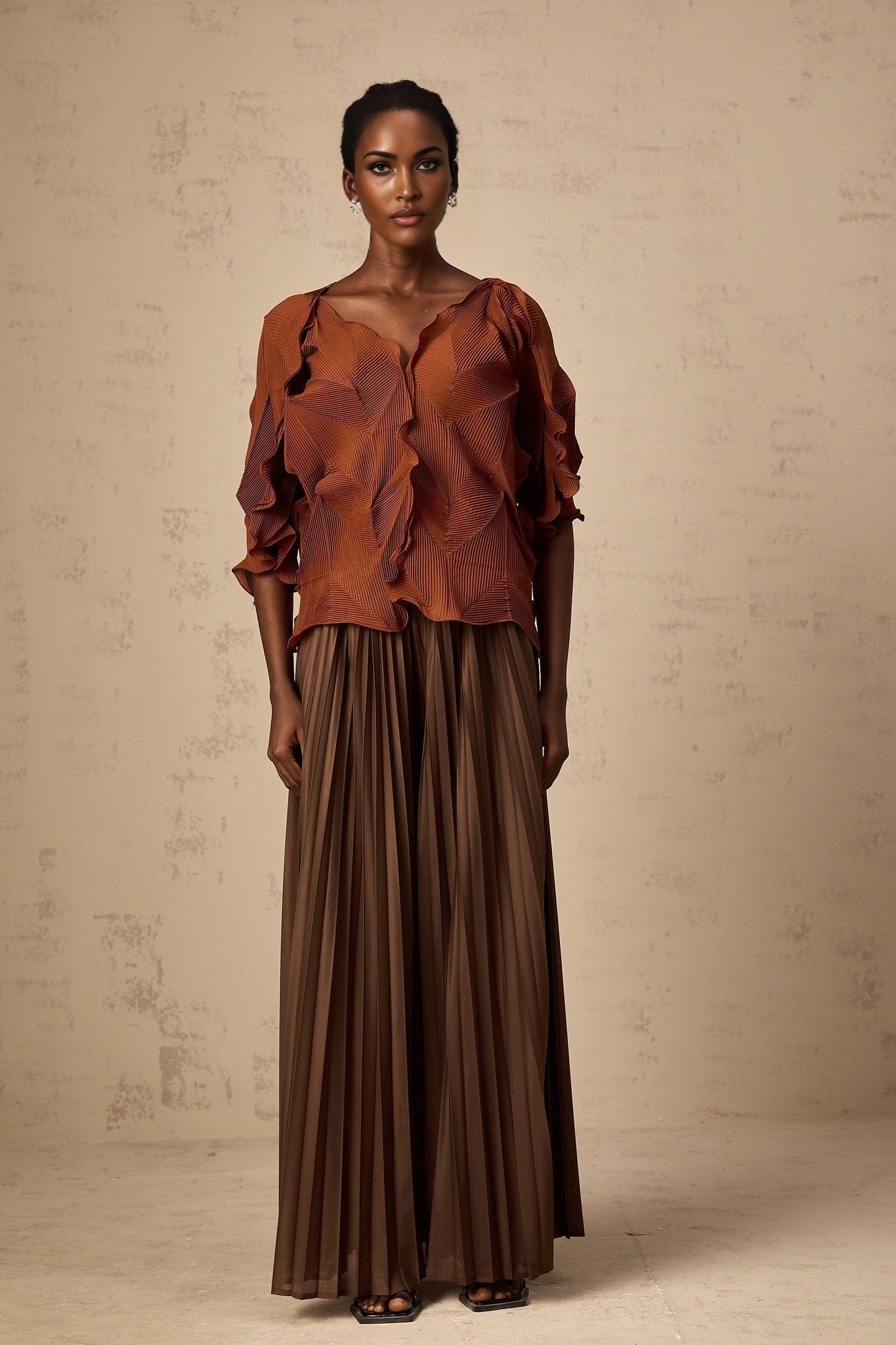 Woman wearing a demi brown matching set with creased texture top and skirt standing against plain background