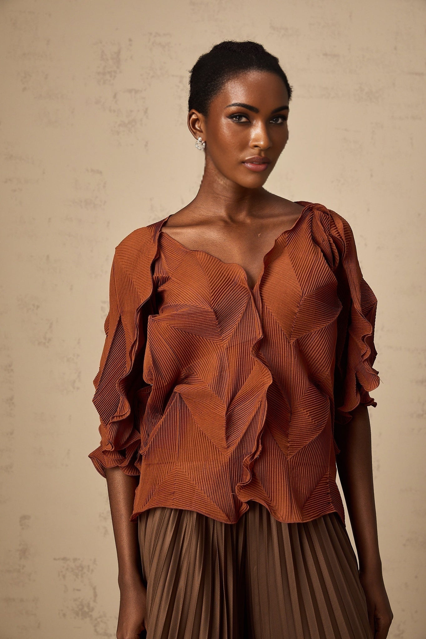 Woman wearing a demi brown matching set with creased top and skirt standing against plain background