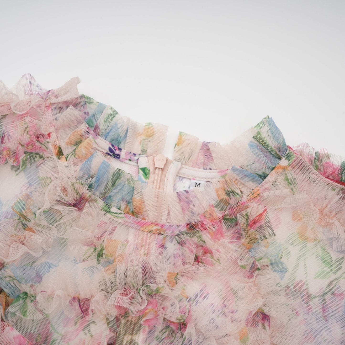 Woman wearing a floral patterned midi dress with ruffled details and tulle overlay in soft pastel colors