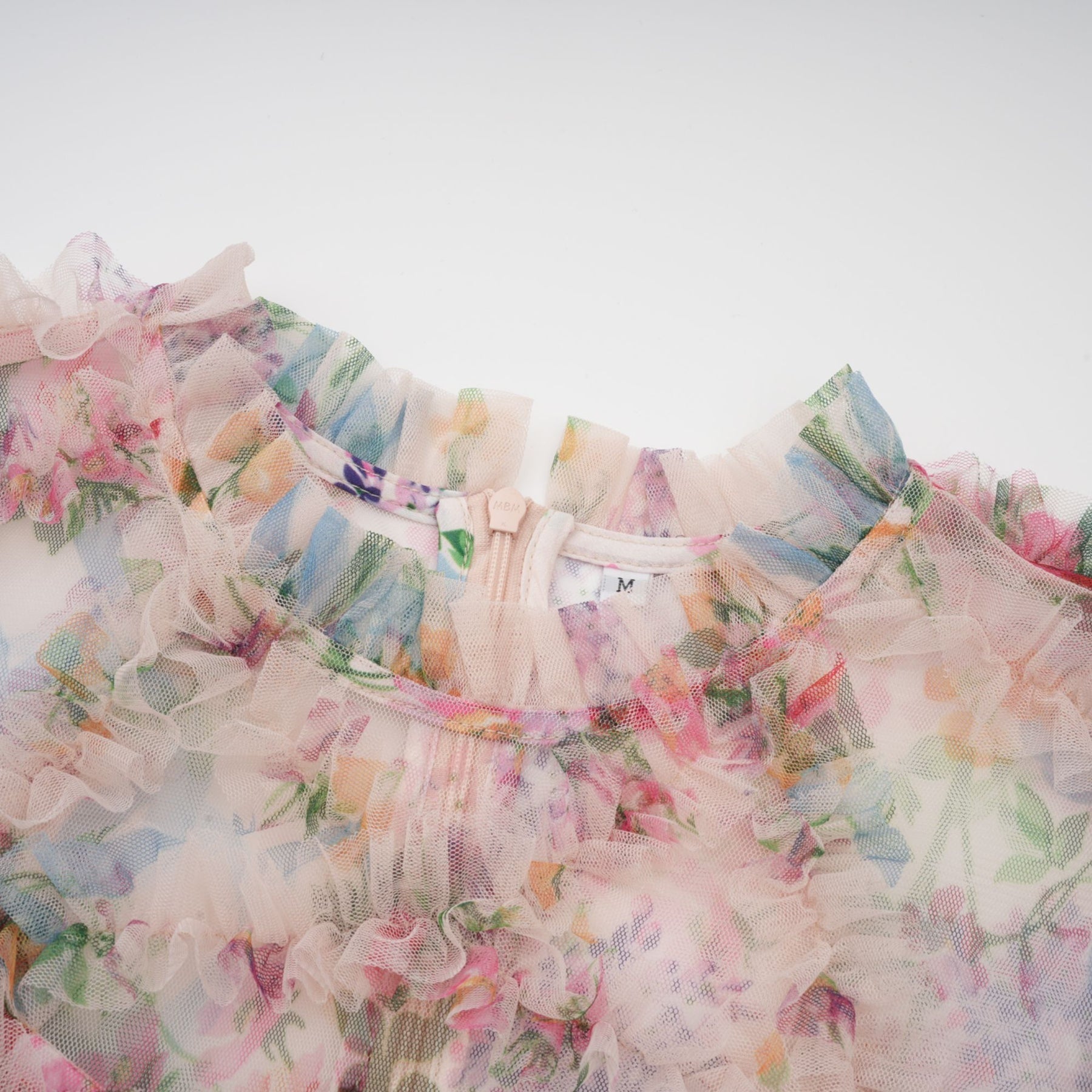 Woman wearing a floral patterned midi dress with ruffled details and tulle overlay in soft pastel colors
