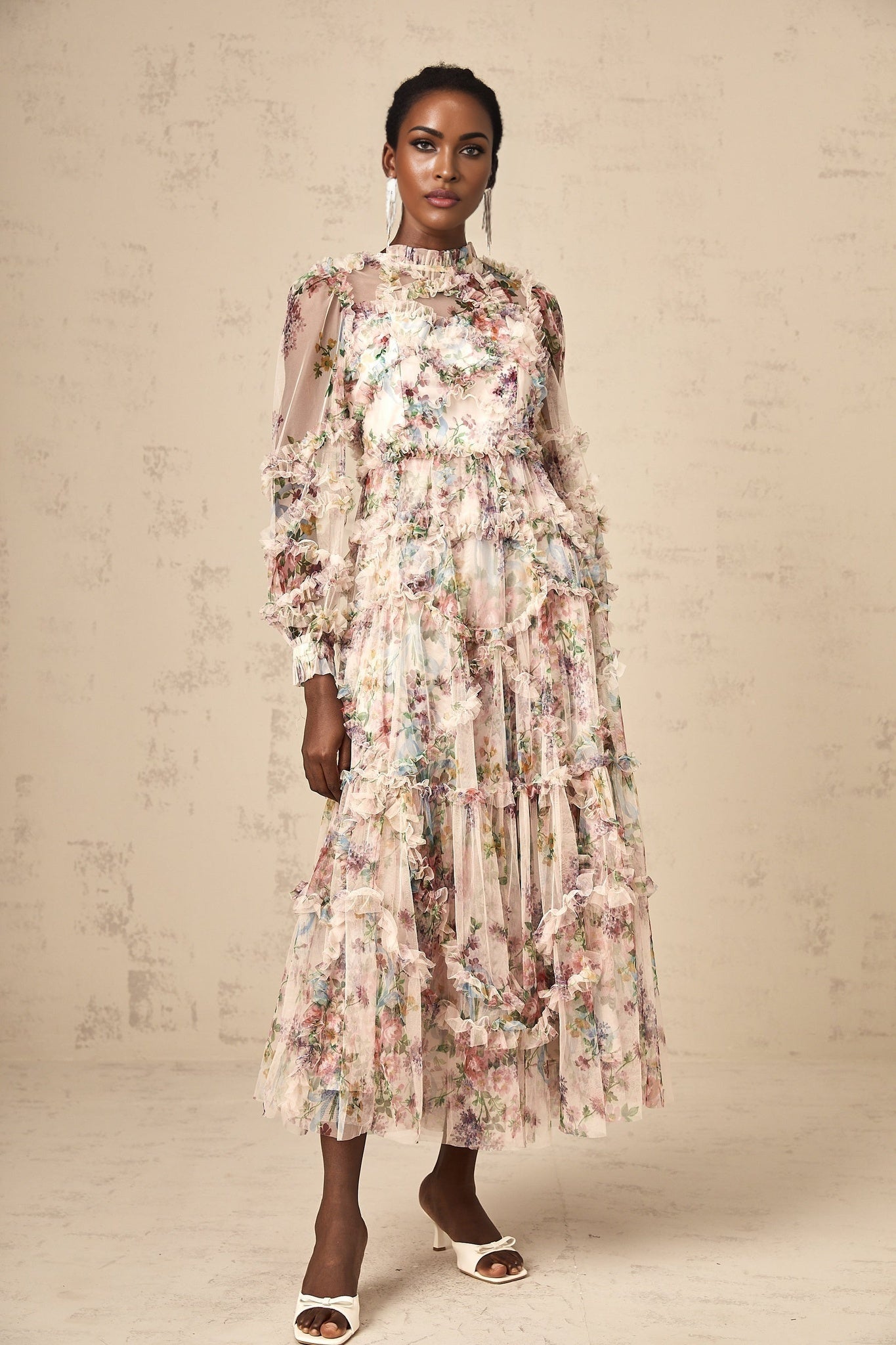 Woman wearing a floral patterned midi dress with ruffles and tulle fabric standing in a neutral background