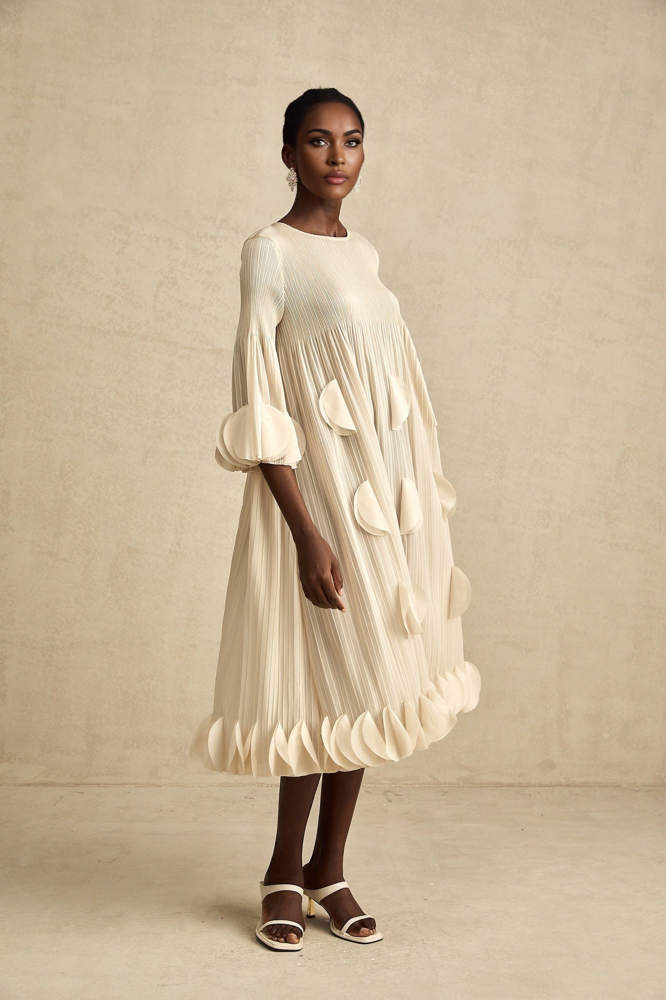 Woman wearing a flowing midi dress with three dimensional pleated petal details