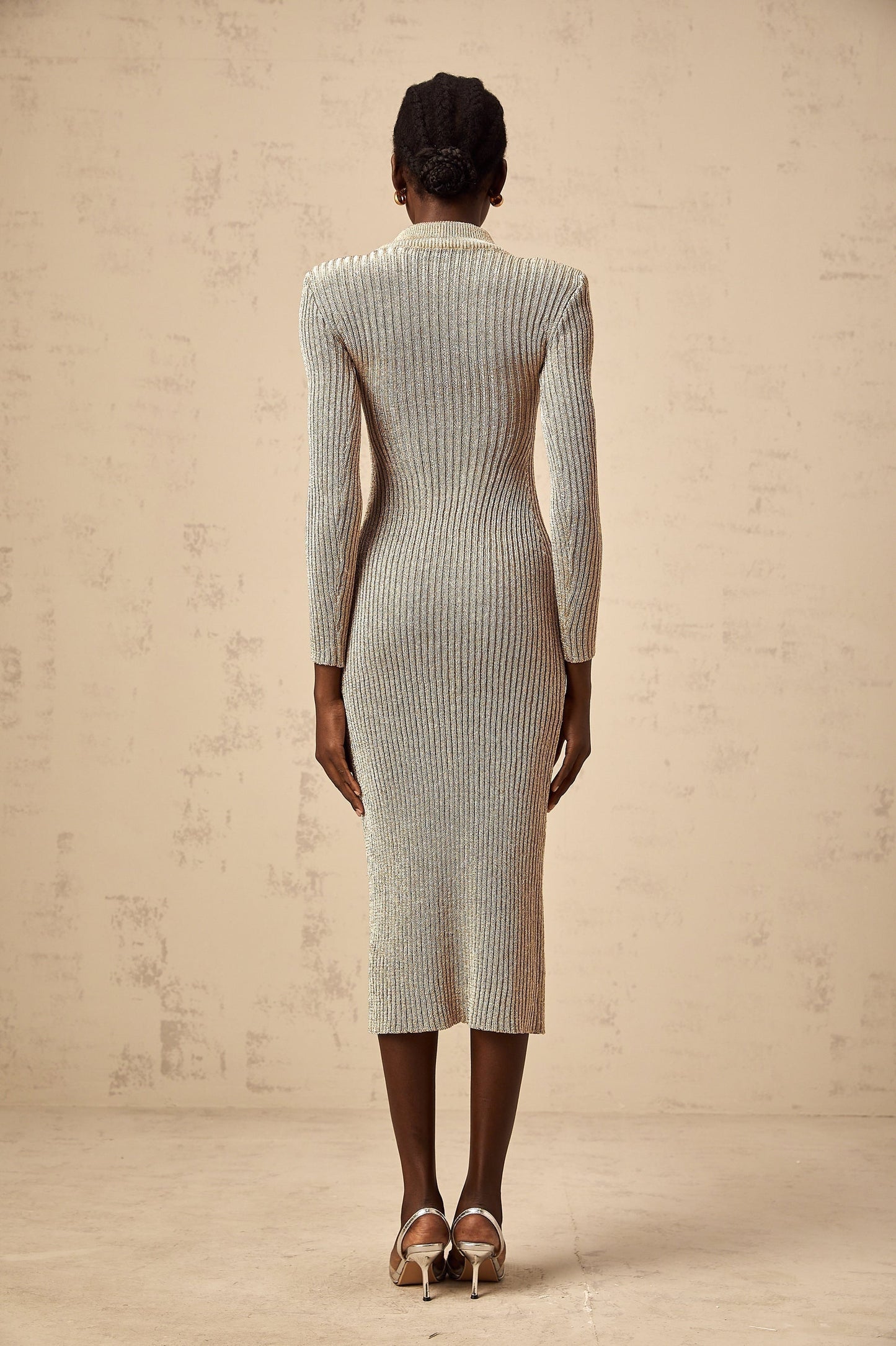 Woman wearing a gold ribbed knit midi dress with pointelle detailing standing in front of a plain background
