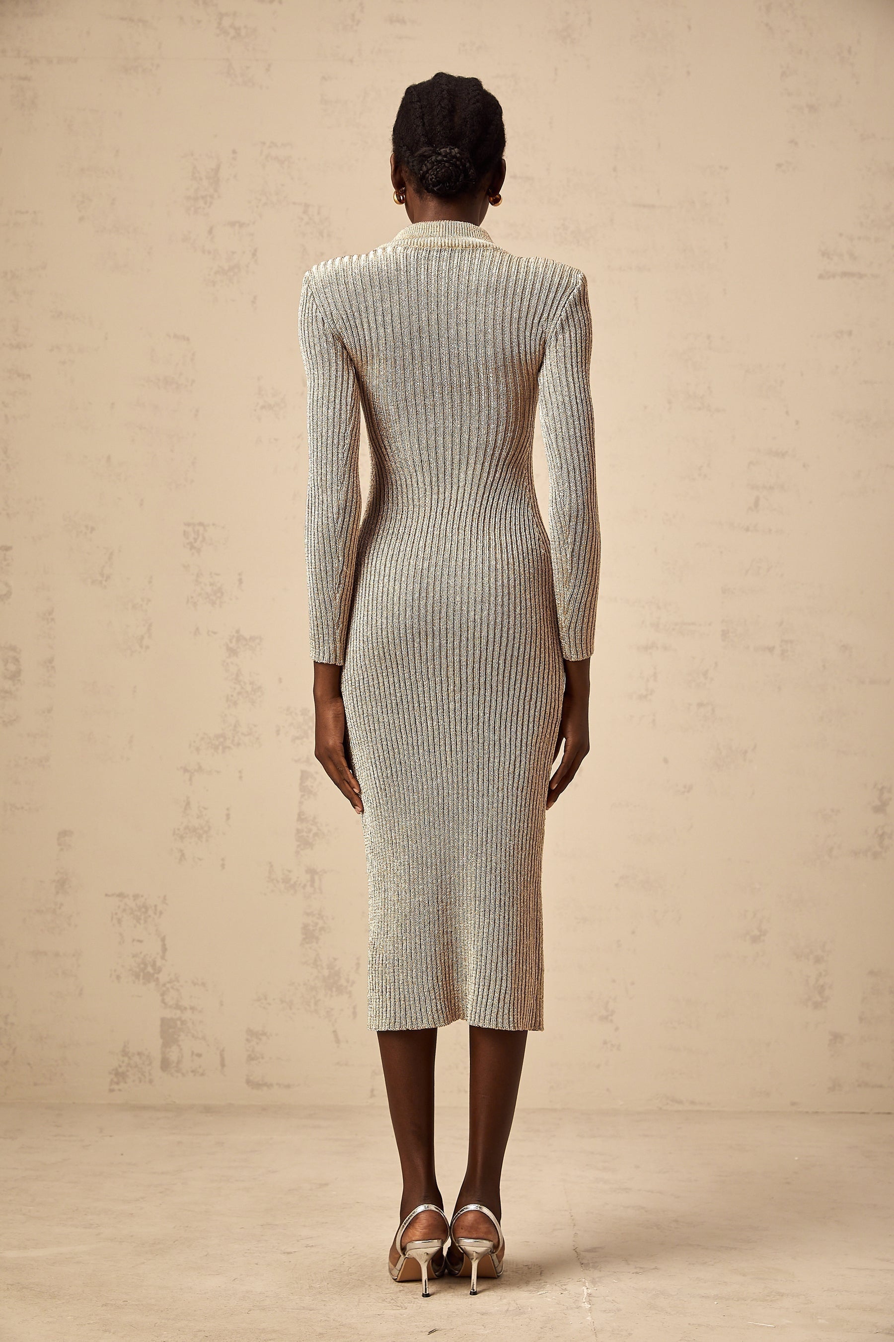 Woman wearing a gold ribbed knit midi dress with pointelle detailing standing in front of a plain background