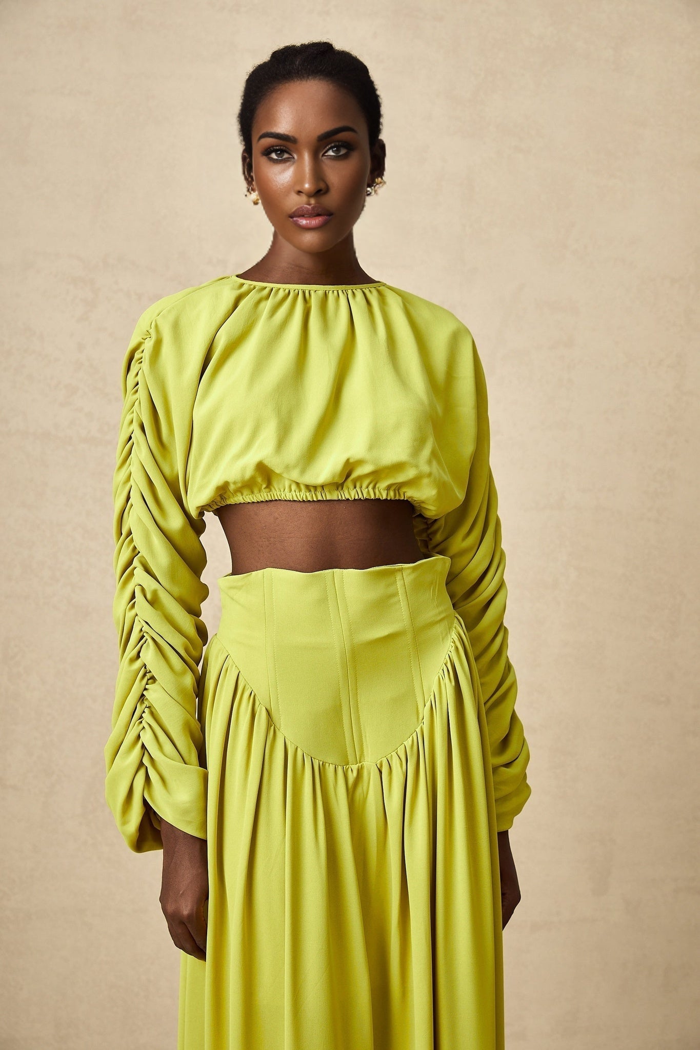 Woman wearing a green twopiece outfit consisting of a smocked top and matching skirt called Émilie